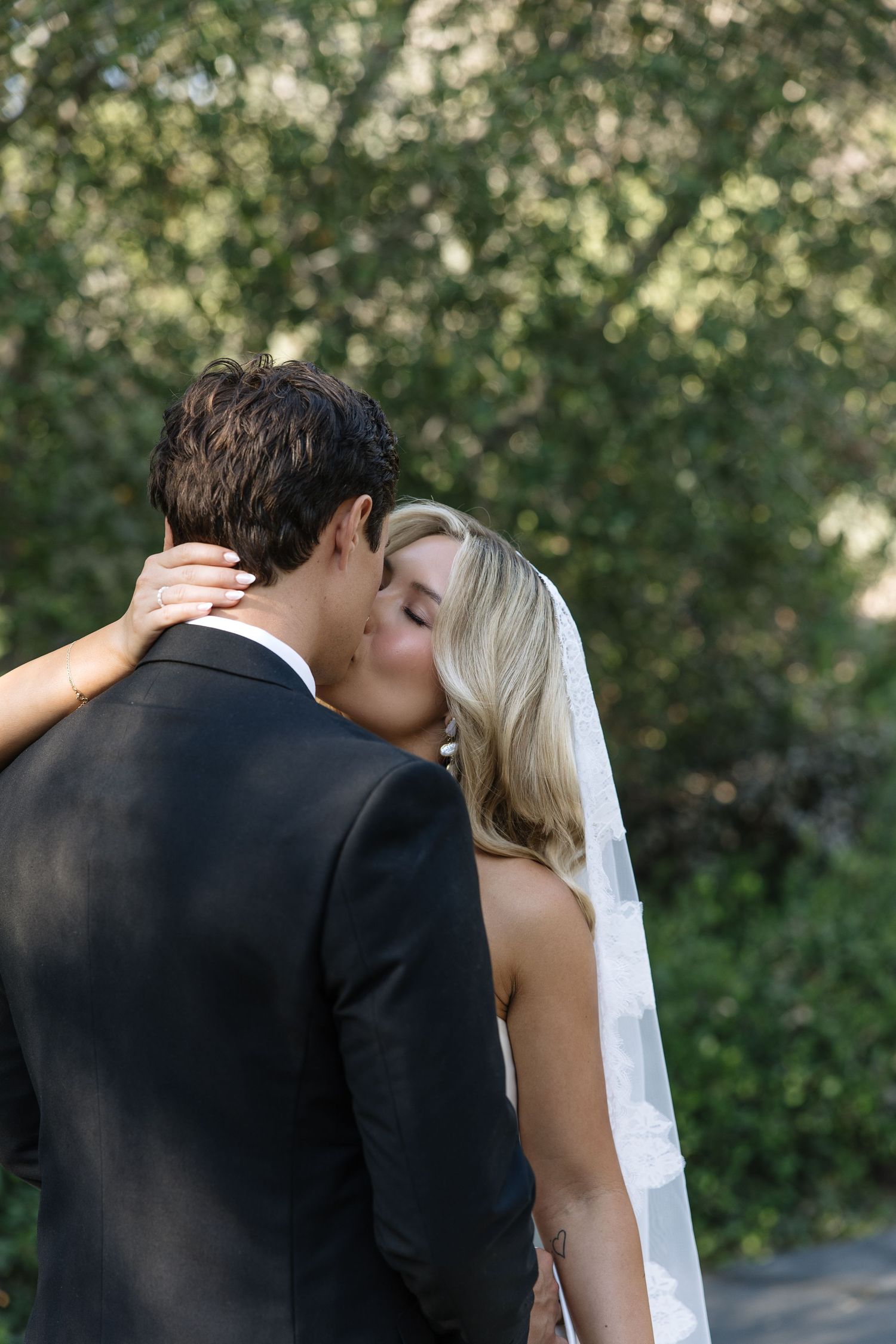 Bride and groom sharing a romantic kiss outdoors, with the bride wearing a white veil and groom in a dark suit.