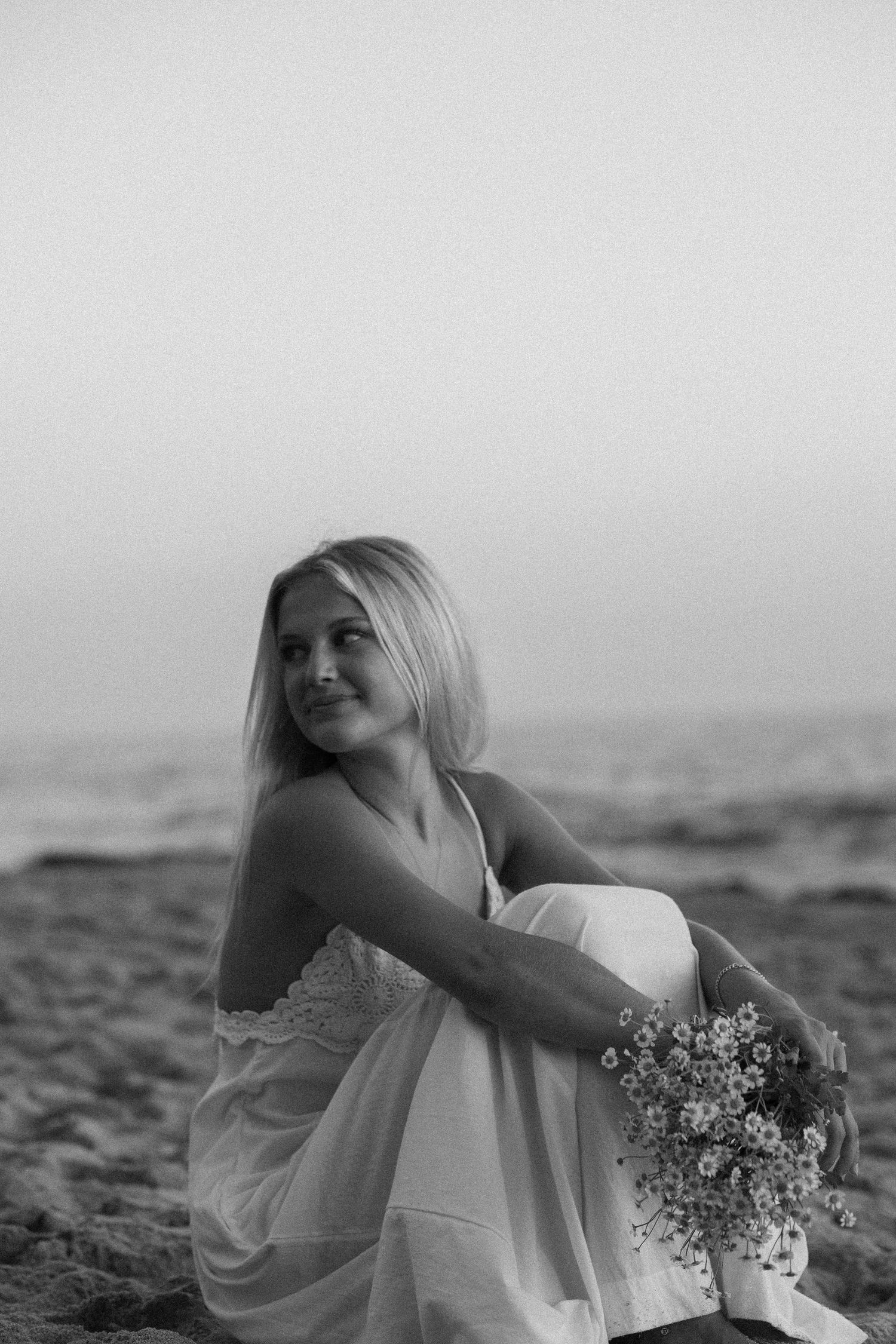 Artistic black and white bridal portraits on beach with flowers.