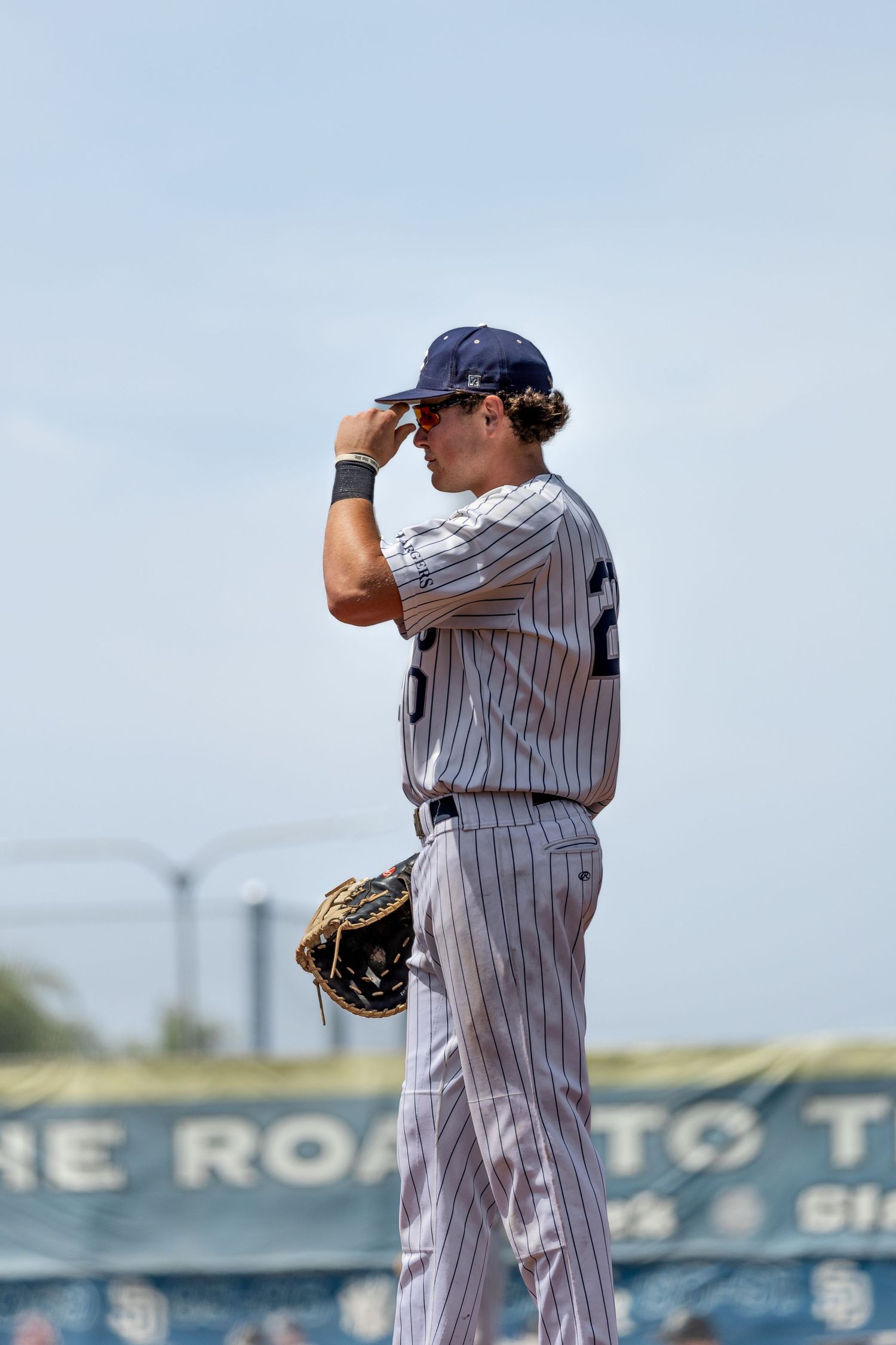 Baseball player in pinstripe uniform adjusting cap on field, holding glove, with stadium banner visible in background.