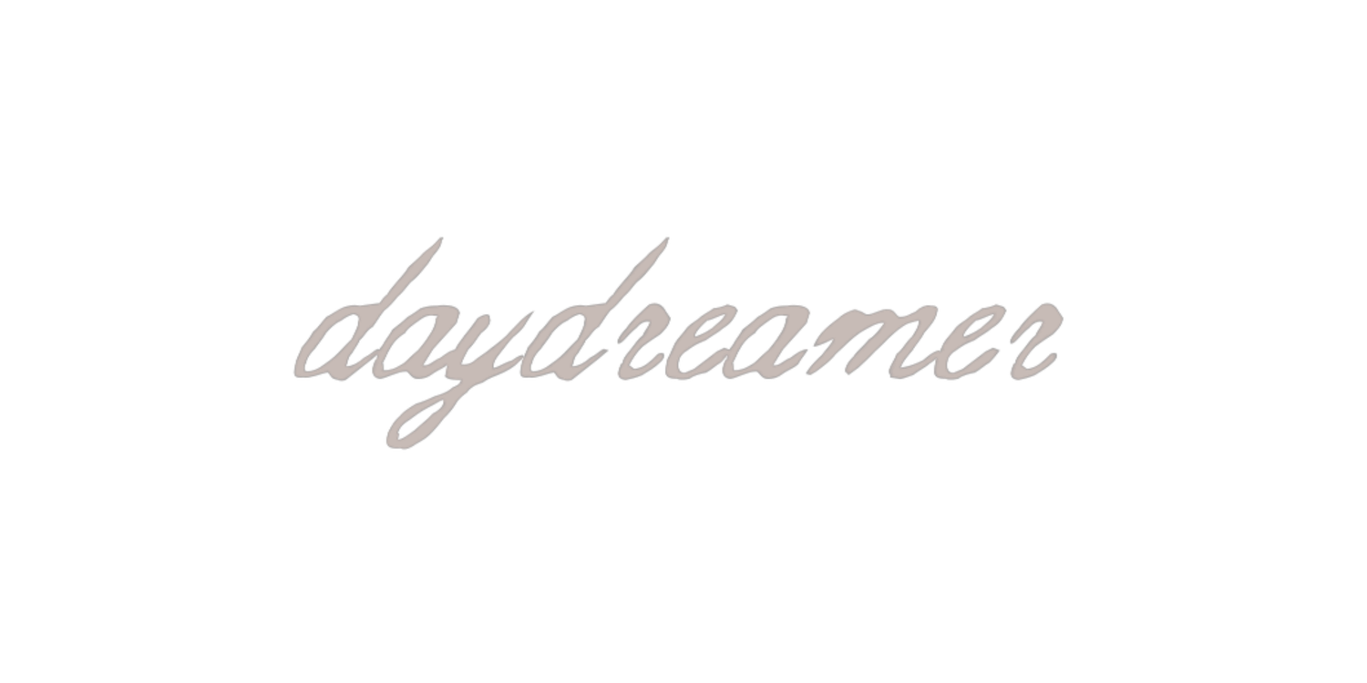Elegant cursive script spelling daydreamer in soft beige tones on a white background.