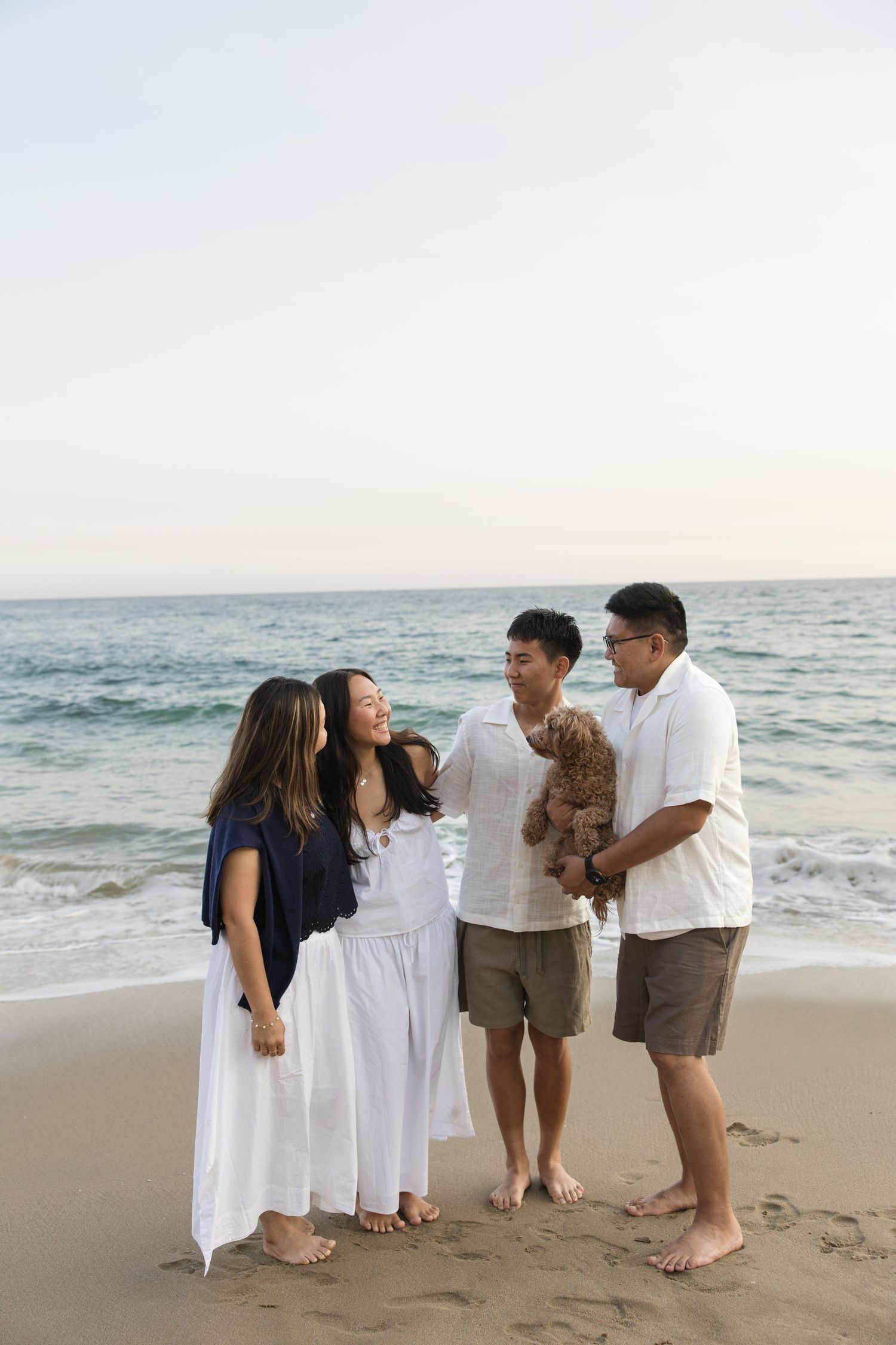 Happy Asian family of four with a small dog enjoying a sunset beach outing together.