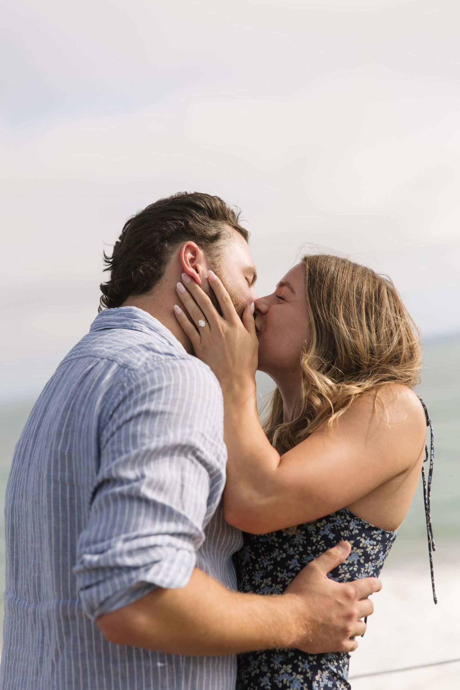 Romantic couple sharing a passionate kiss outdoors near the ocean, embracing each other on a cloudy day.