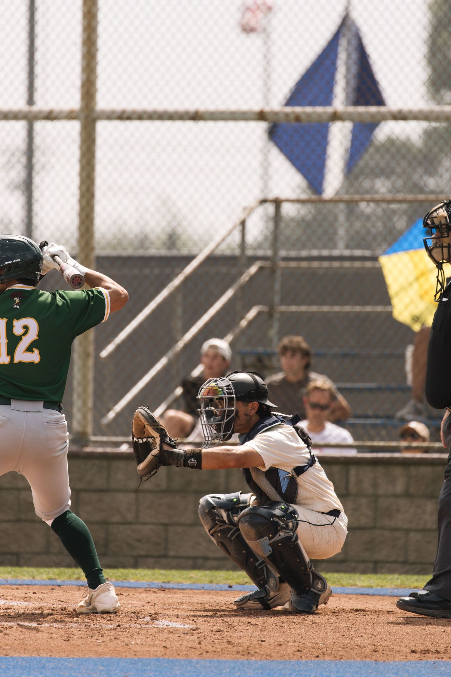 Baseball batter in green jersey number 12 swings at pitch while catcher crouches and umpire watches during game.
