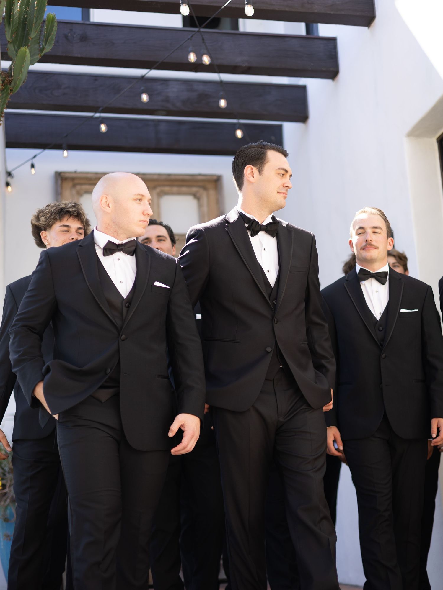 Groomsmen in classic black tuxedos lined up at wedding venue.