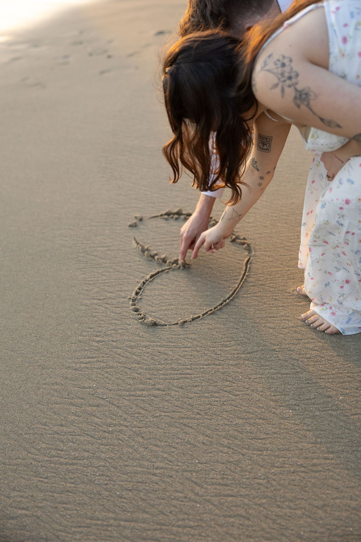 Someone drawing a heart shape in wet sand on the beach.