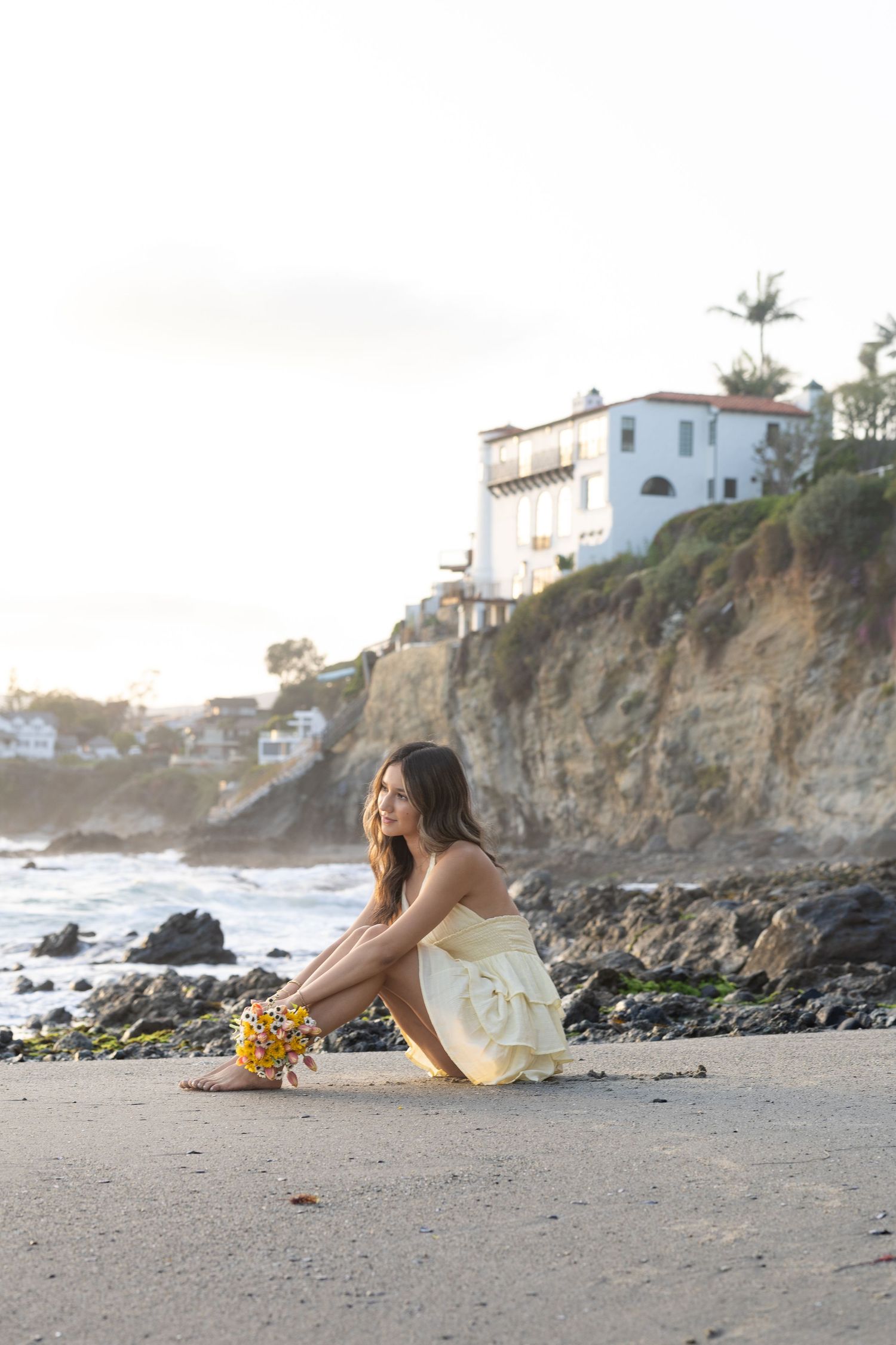 Sunset beach photo with coastal cliffs and white dress against golden light.