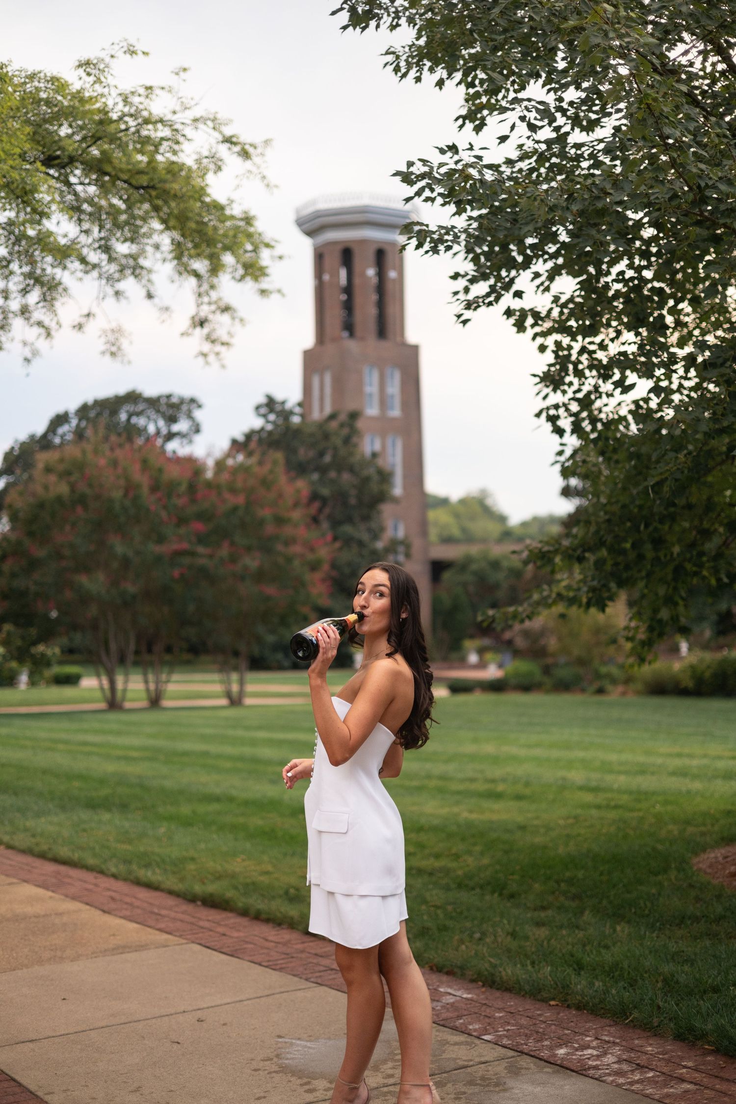 White dress against campus backdrop with iconic bell tower visible through trees.