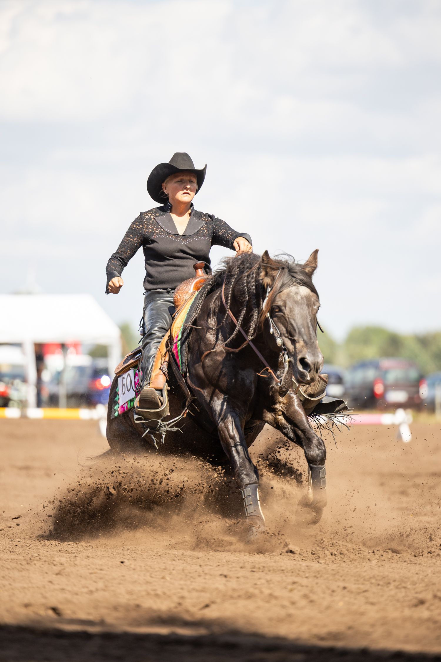 Horse and rider performing a dramatic sliding stop in dusty arena during western competition.