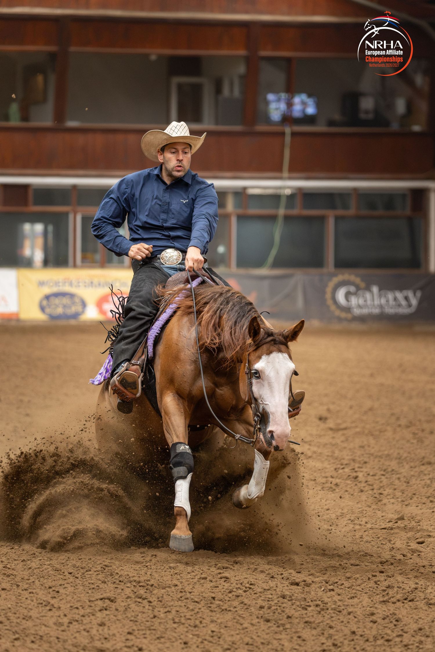 Cowboy riding a chestnut horse performing a sliding stop in a reining competition at an NRHA event.