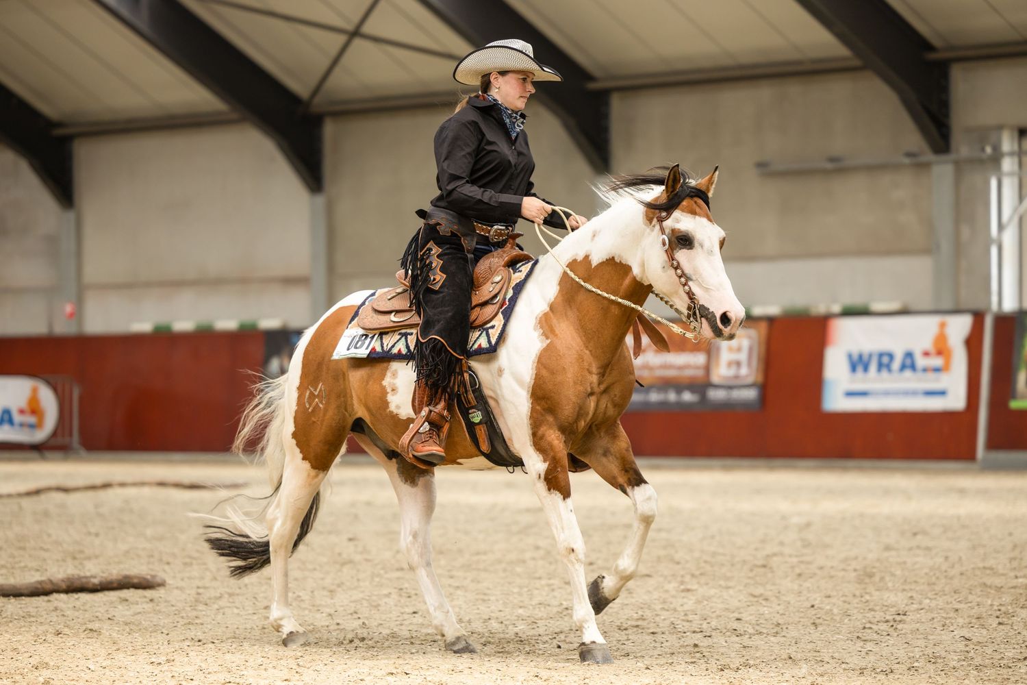 Paint horse and rider performing a western riding pattern in an indoor arena.