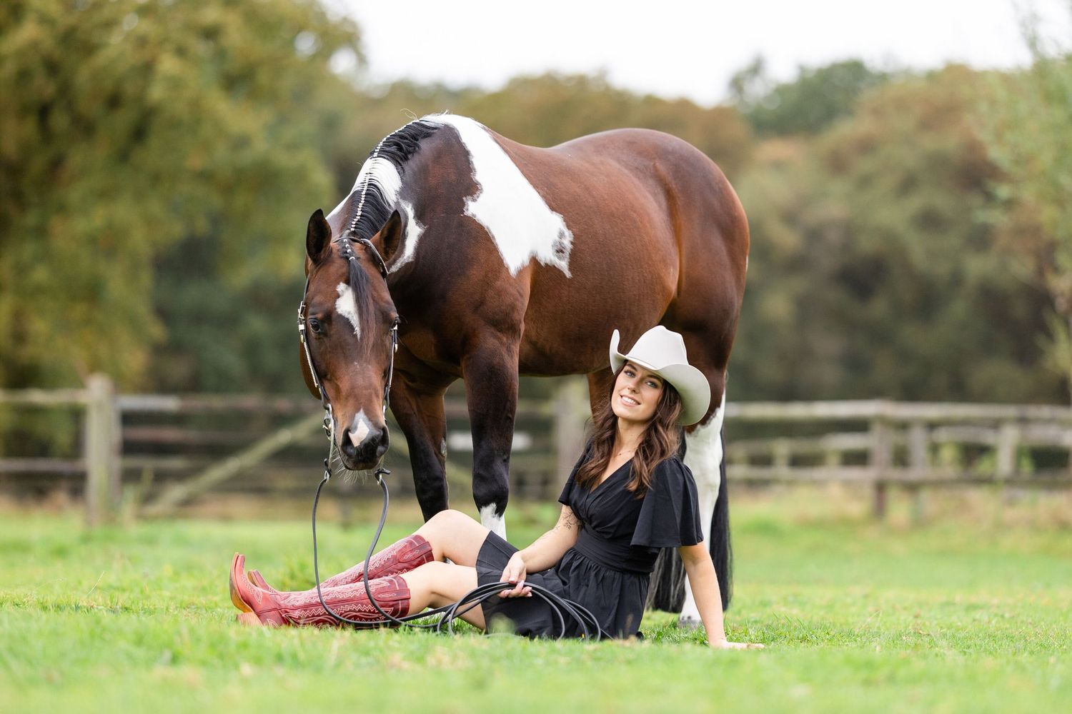 Paint horse and rider relaxing together in a grassy field with wooden fencing in the background.
