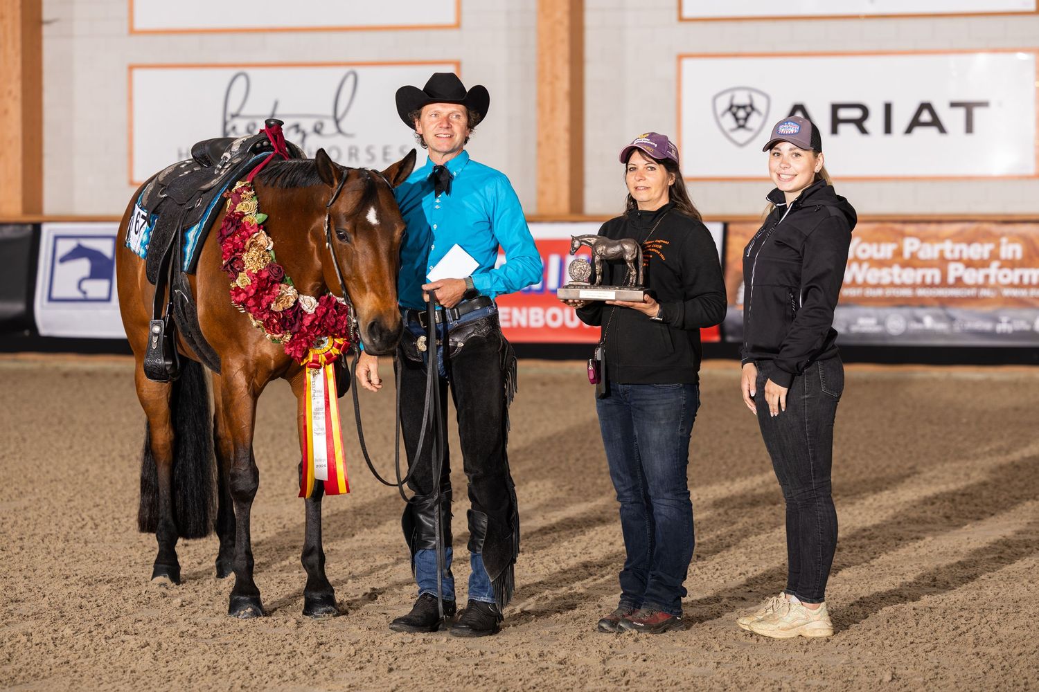 Equestrians and horses lined up in an indoor arena with sponsor banners visible on the walls.