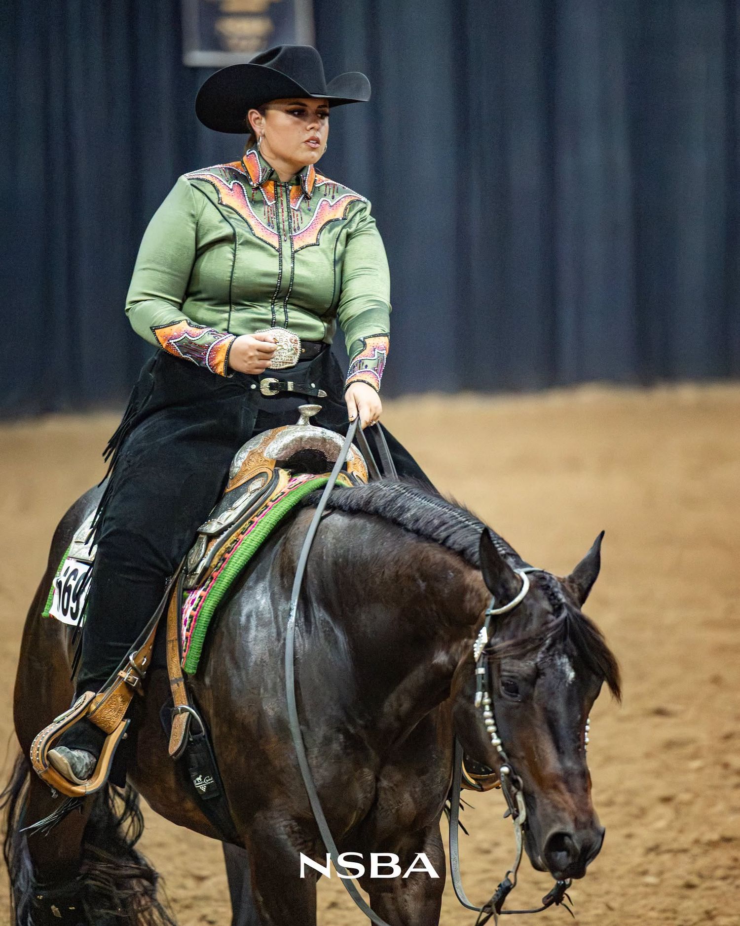 Katie van Slyke in a green western shirt and black cowboy hat rides a dark horse at the NSBA World Show