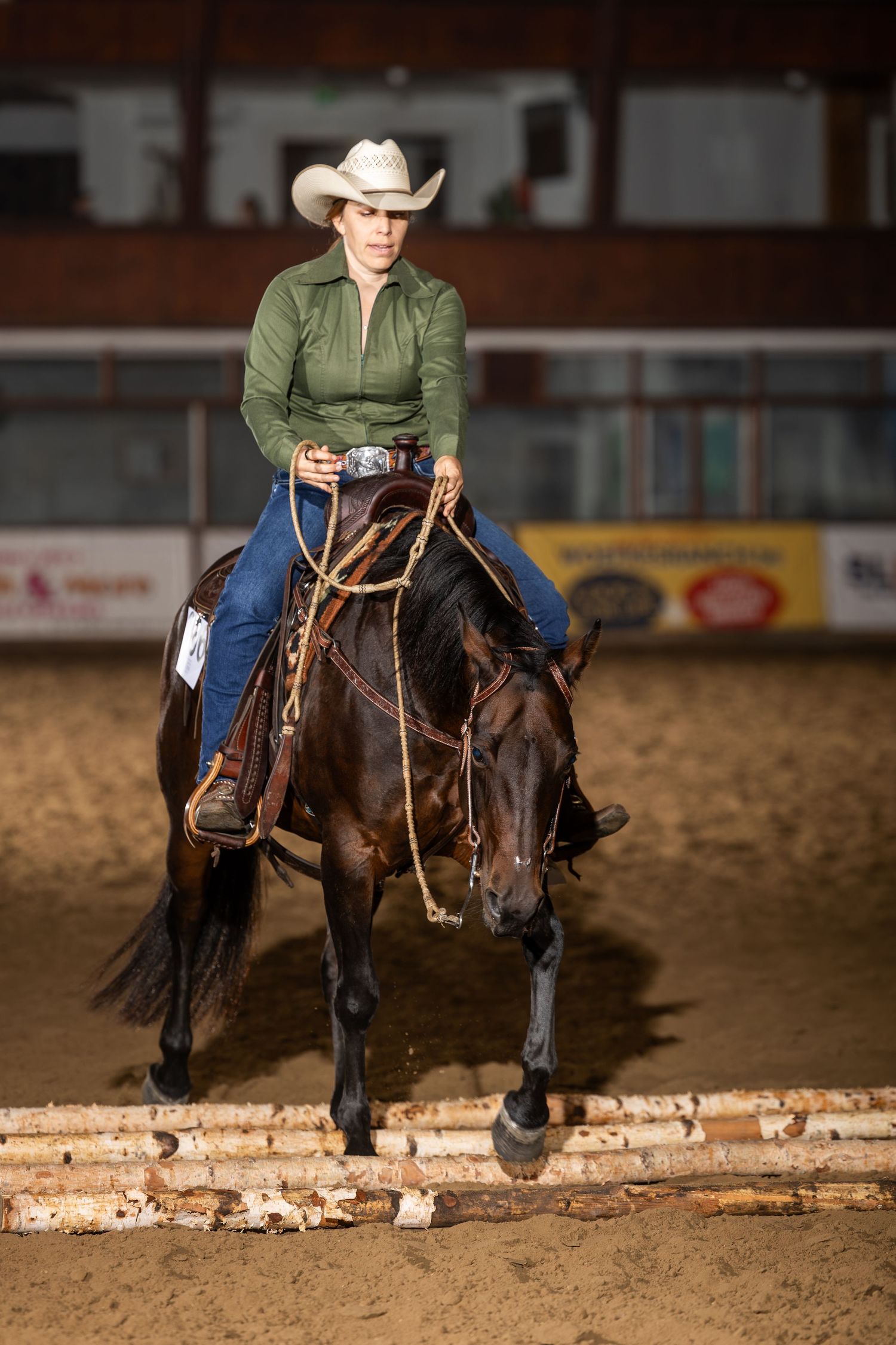 Woman in cowboy hat riding dark horse in indoor arena during western equestrian competition.