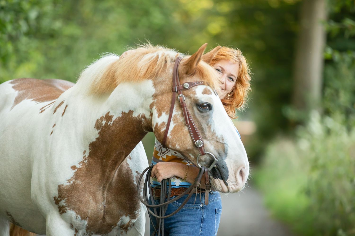 Close-up view of a paint horse with distinctive brown and white markings against green foliage.
