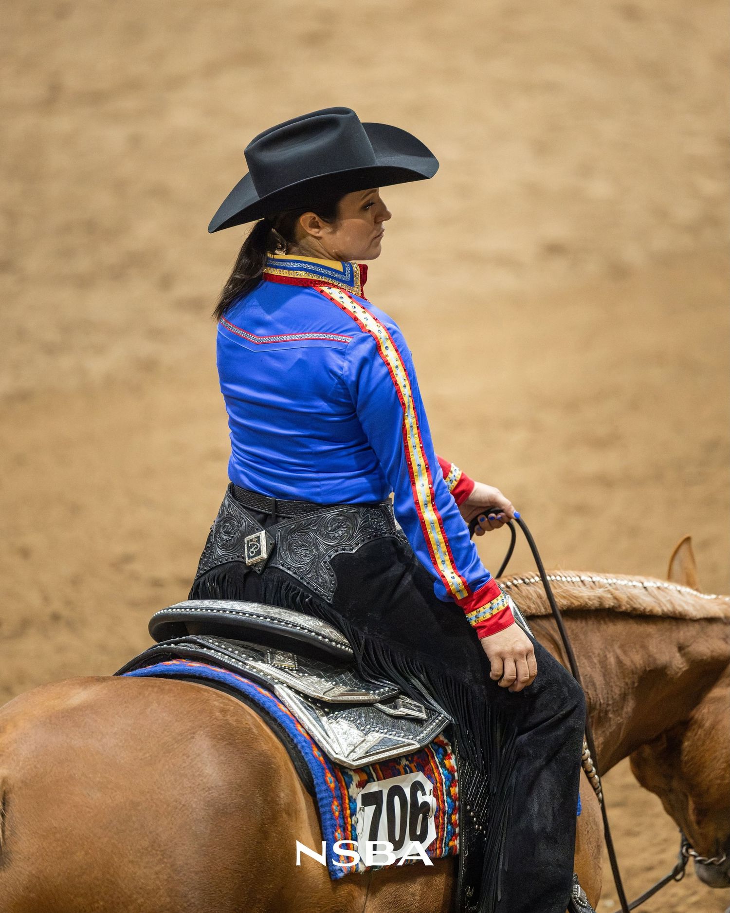 Female equestrian in blue jacket and black cowboy hat rides horse at NSBA World Show, backnumber 706.