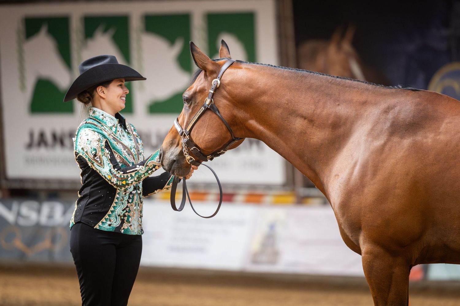 Woman in western show attire presenting a chestnut horse at an indoor equestrian show competition.