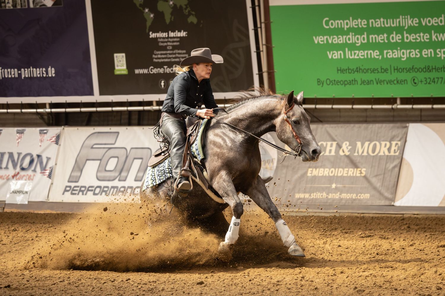 A horse and rider perform a sliding stop maneuver in a dirt arena during a western reining competition.