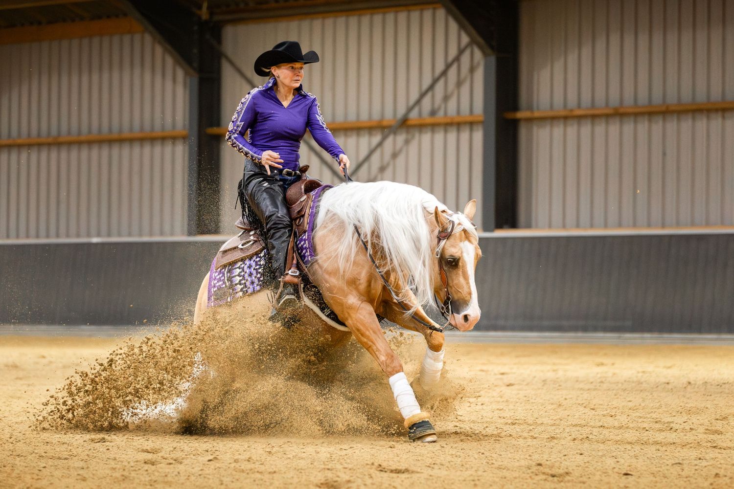 Reining horse and rider performing sliding stop maneuver with sand flying.