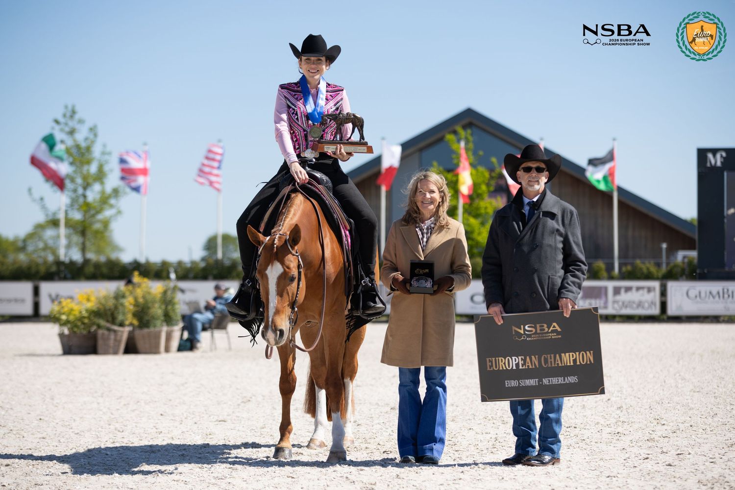 NSBA European Champion equestrian winner on horseback with two presenters holding championship plaque at outdoor arena.