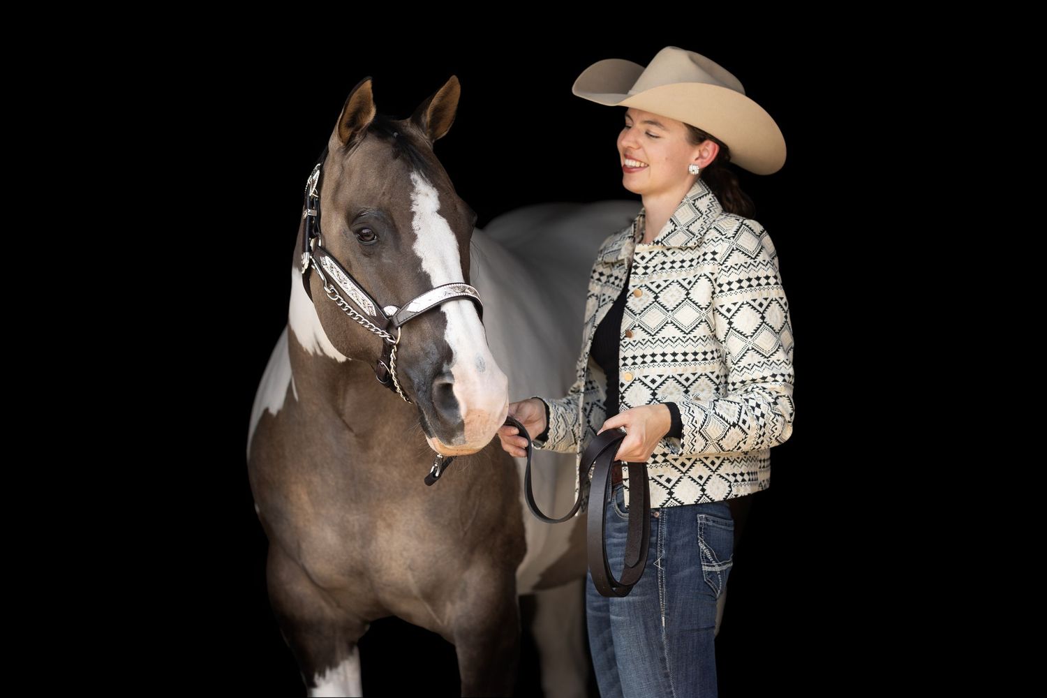 A paint horse and rider in western attire pose together against a black background.