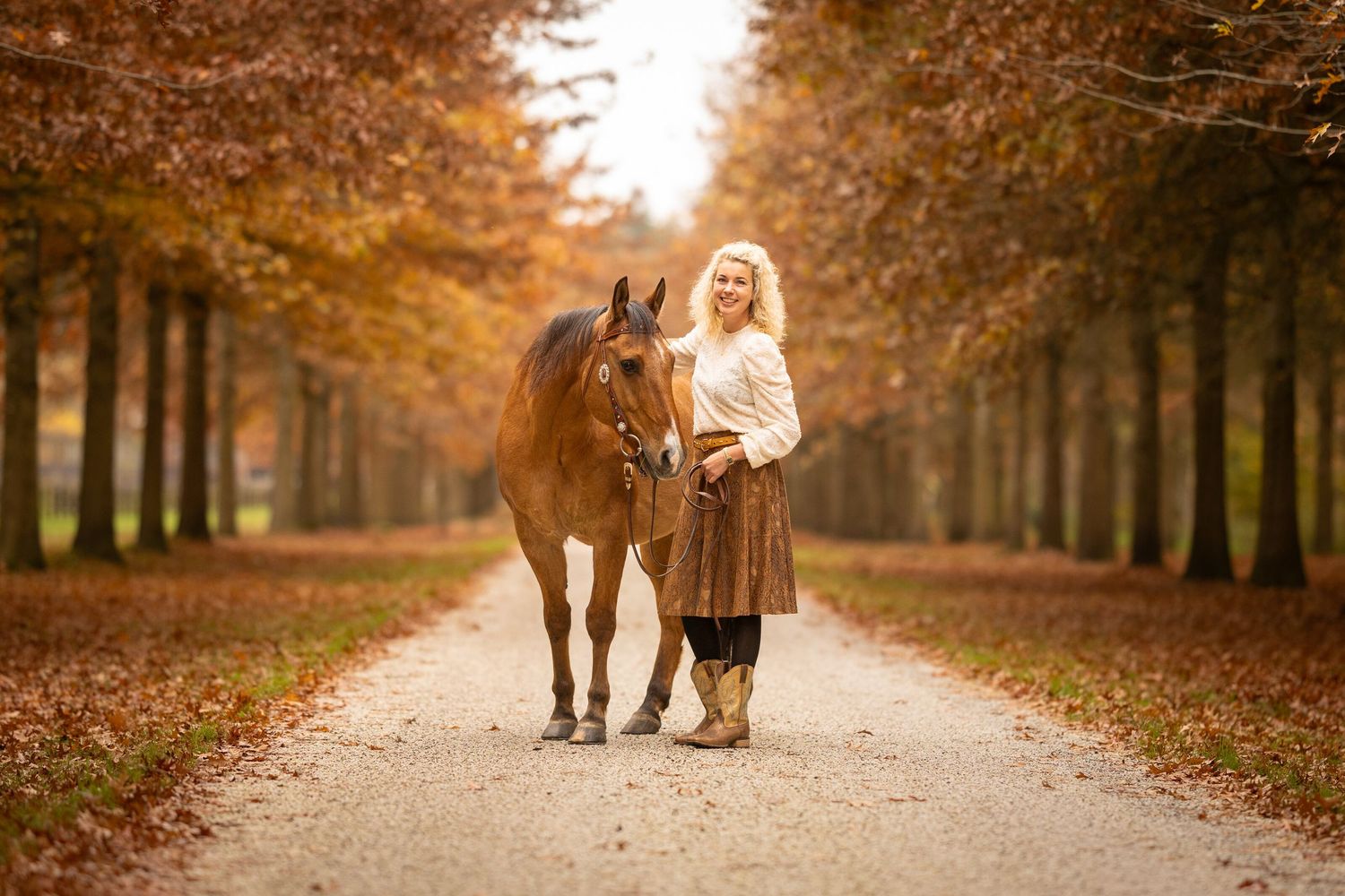 Person and horse walking together on tree-lined path during autumn season.