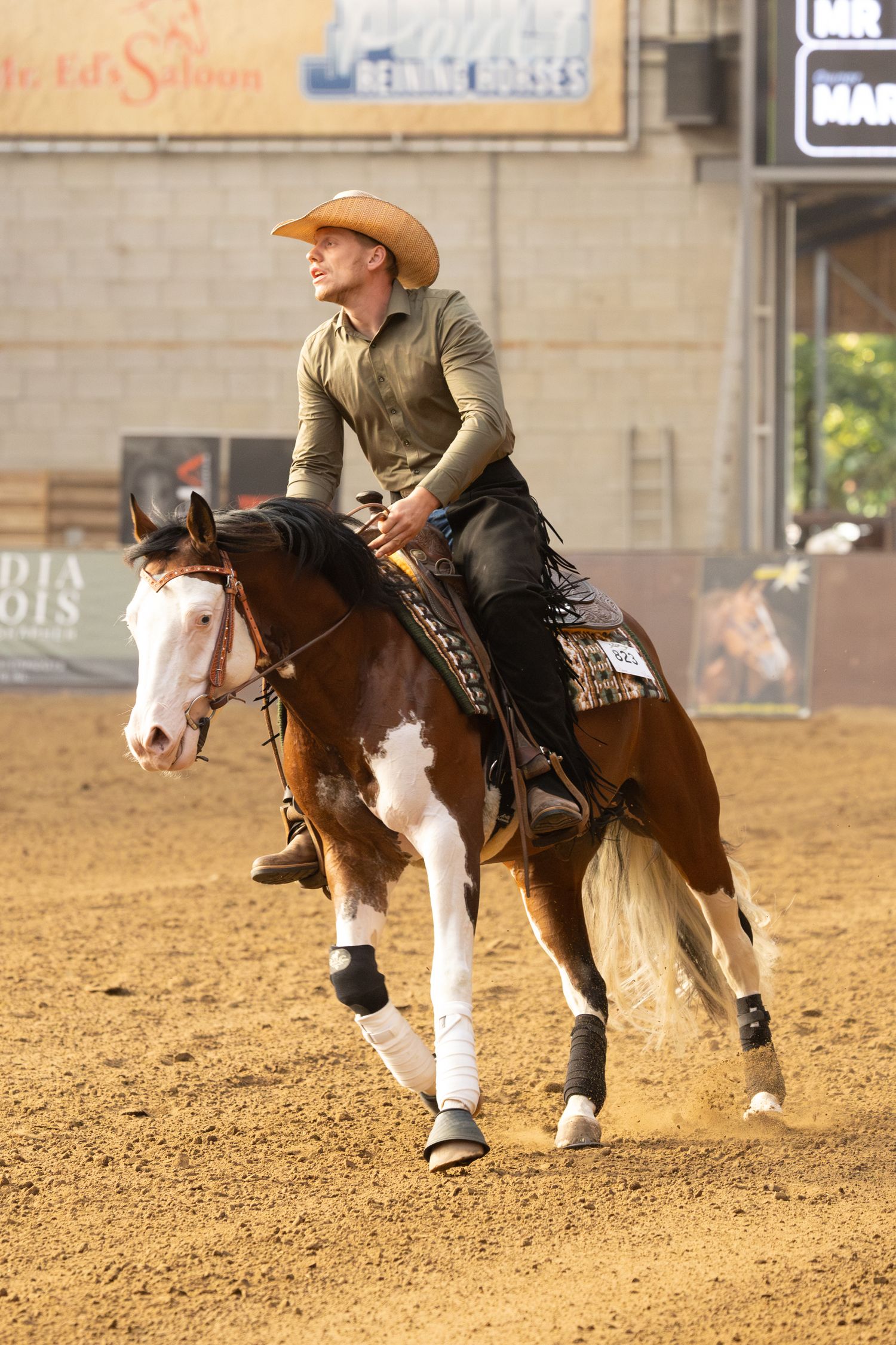 Rider in cowboy hat and tan shirt riding a paint horse during western competition.