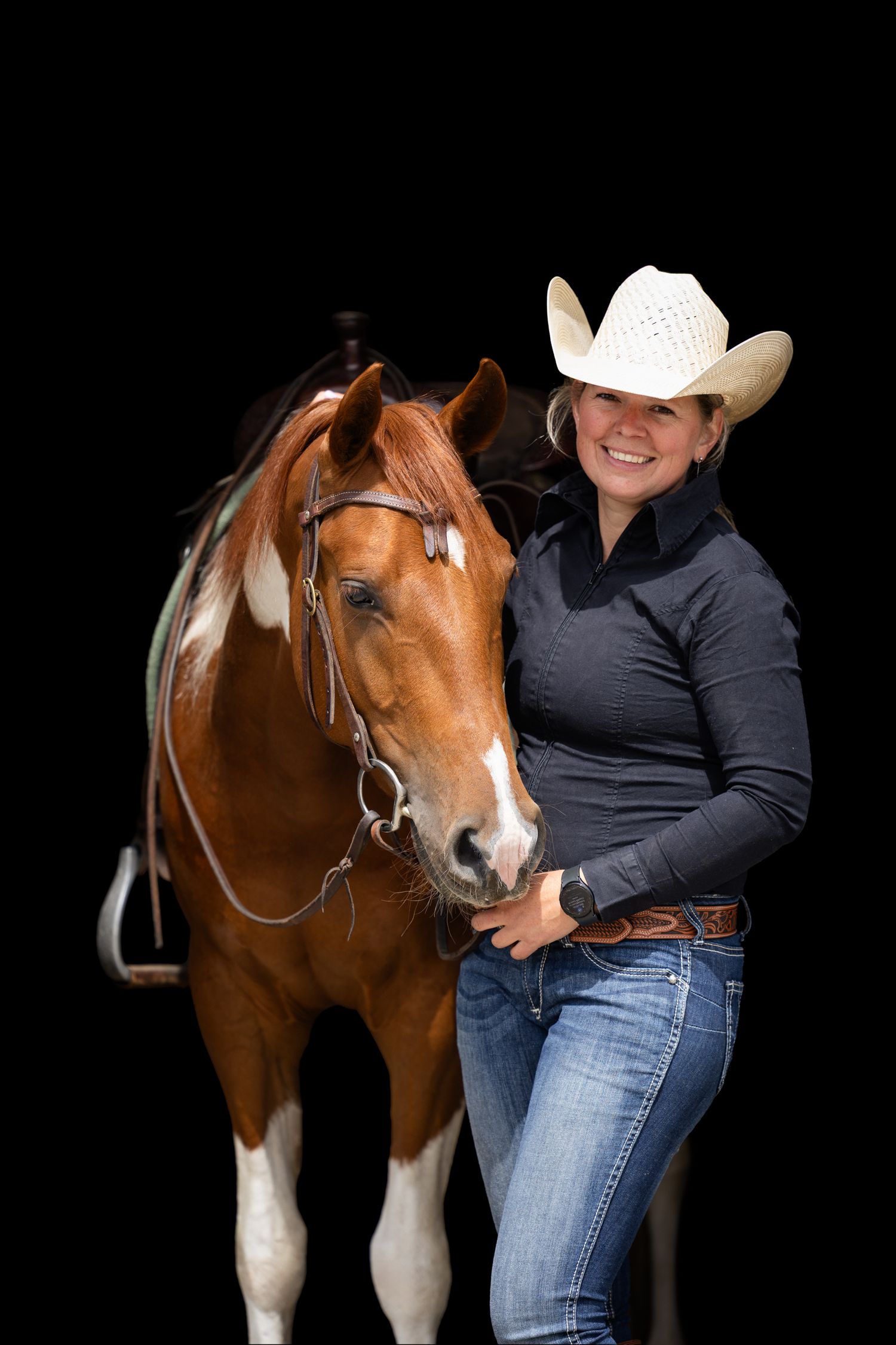 A chestnut and white horse with rider stands against a black background in a studio setting.