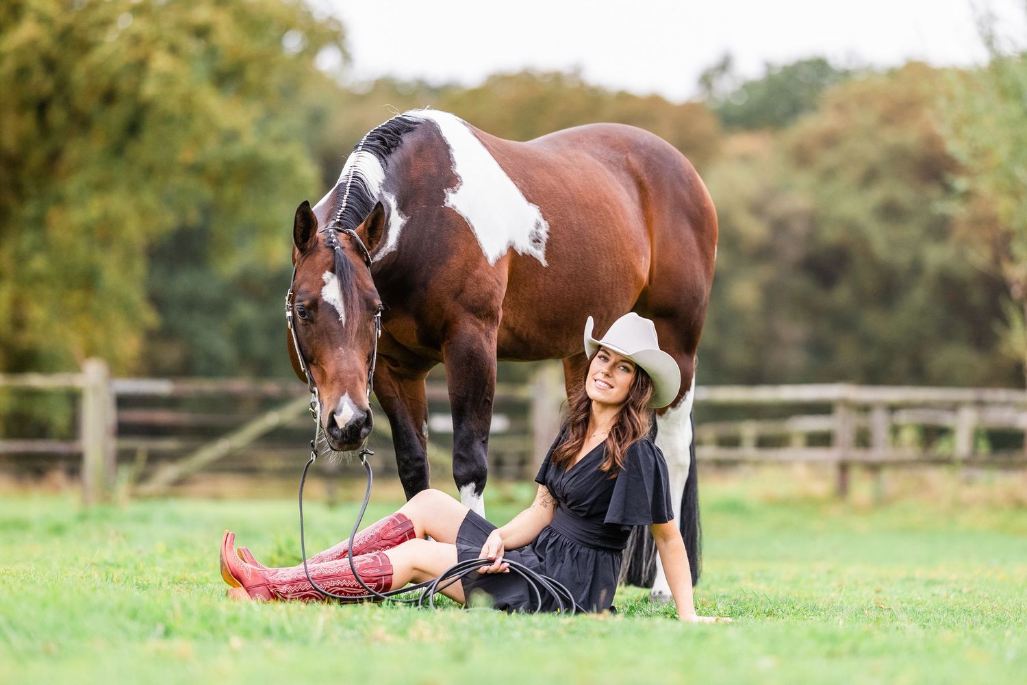 Horse being led through grassy field with autumn foliage in background.