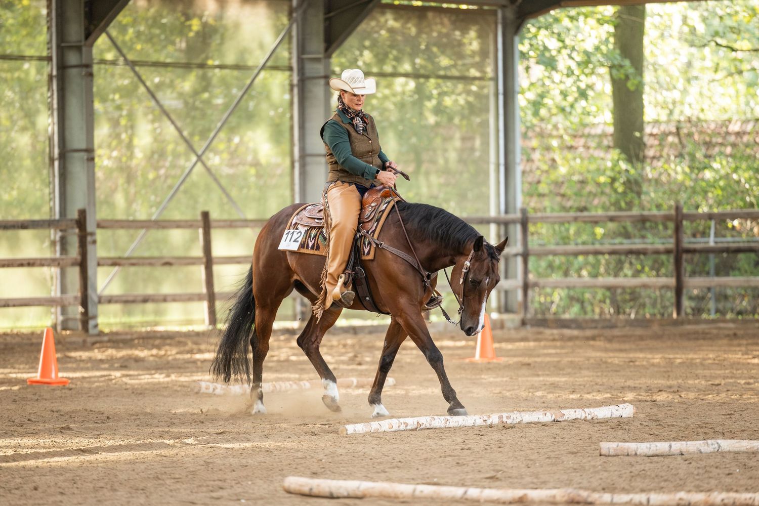Rider in cowboy hat on chestnut horse navigating poles in an outdoor western equestrian arena competition.
