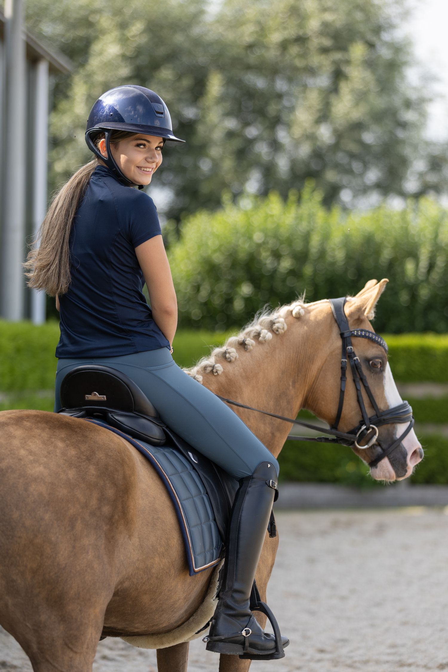 Equestrian rider in navy attire mounted on a brown horse in an outdoor arena.