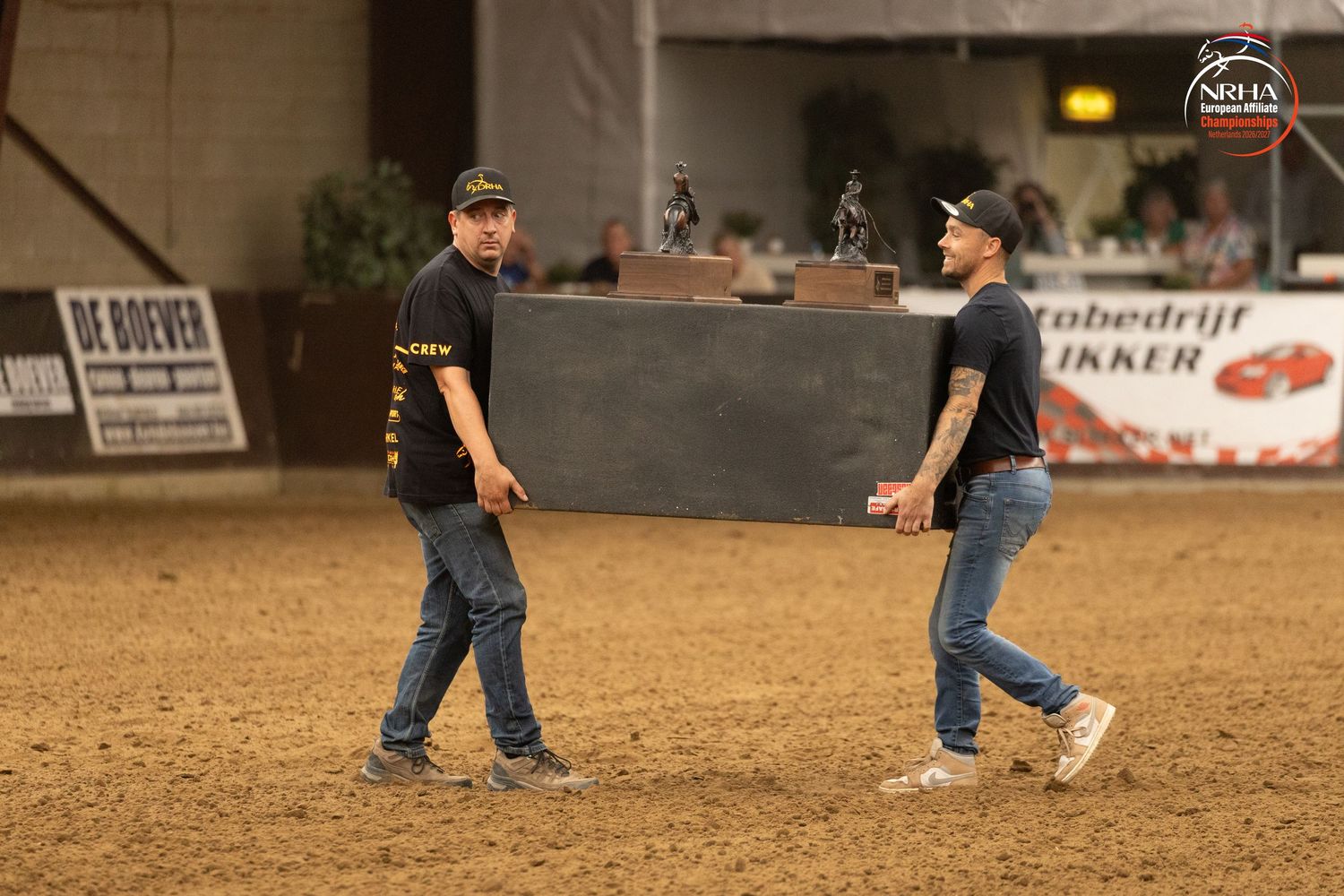 Two men walking in an indoor equestrian arena during a horse show event in the Netherlands.