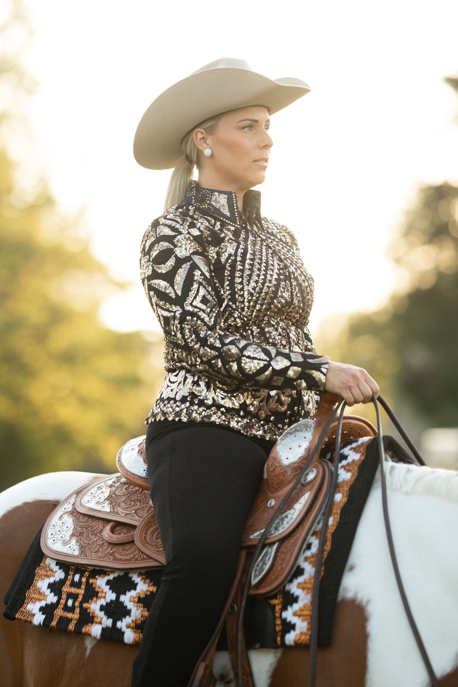 Equestrian rider wearing patterned sweater and cowboy hat on decorated western saddle.