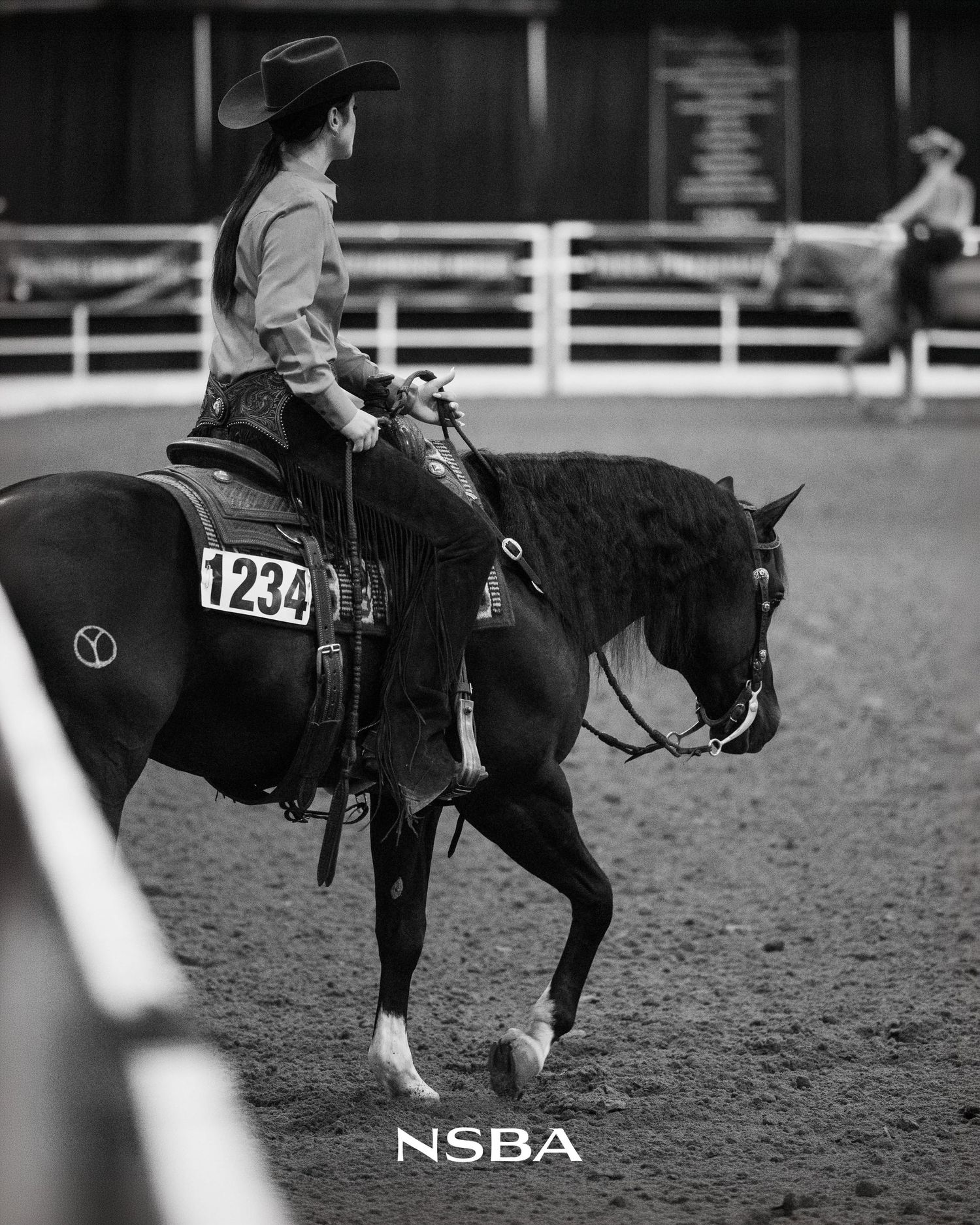 Black and white photo of a rider in cowboy hat on dark horse, numbered 1234, competing at the NSBA World Show
