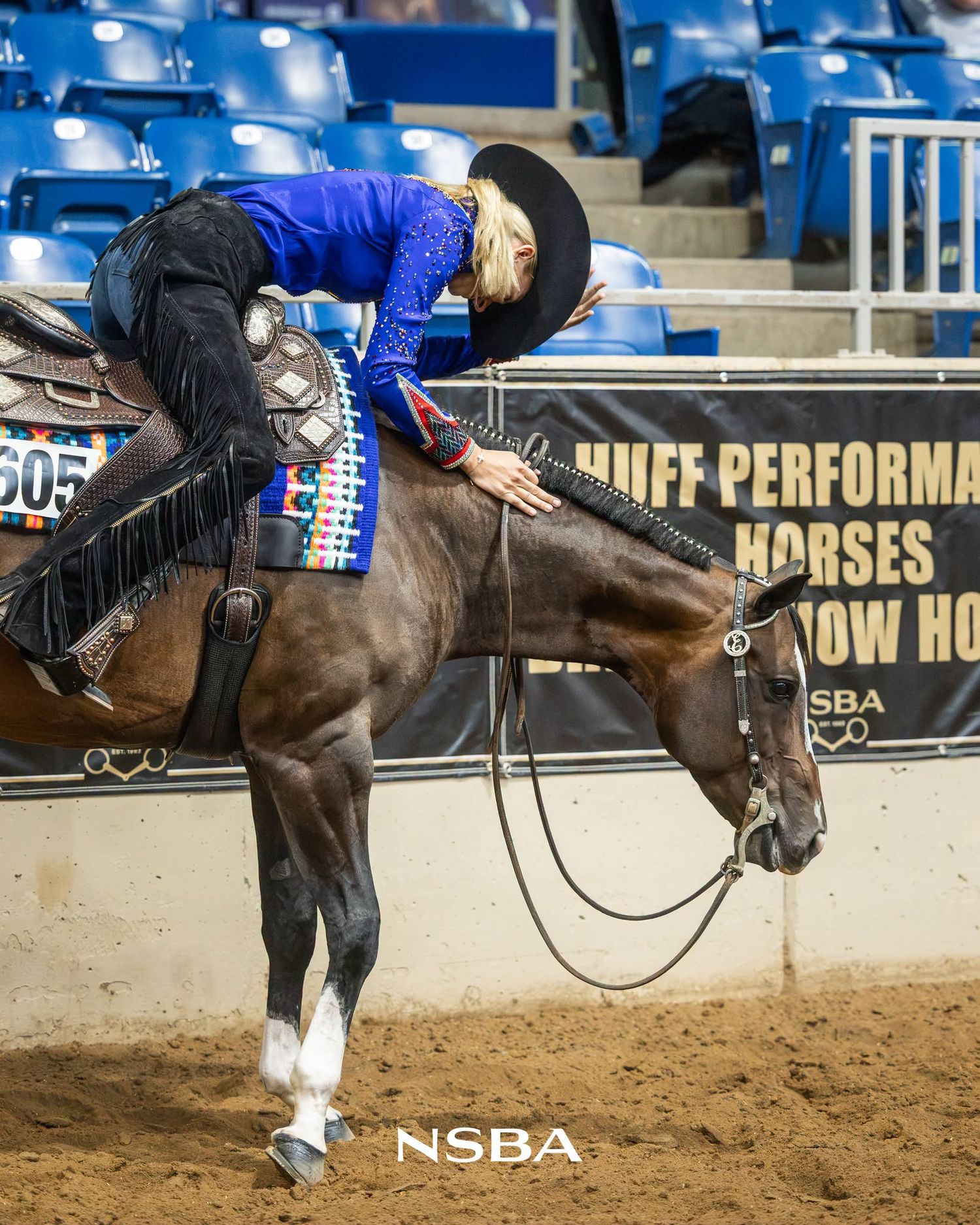 Equestrian rider in blue sequin top and black hat performs with dark horse at NSBA competition.