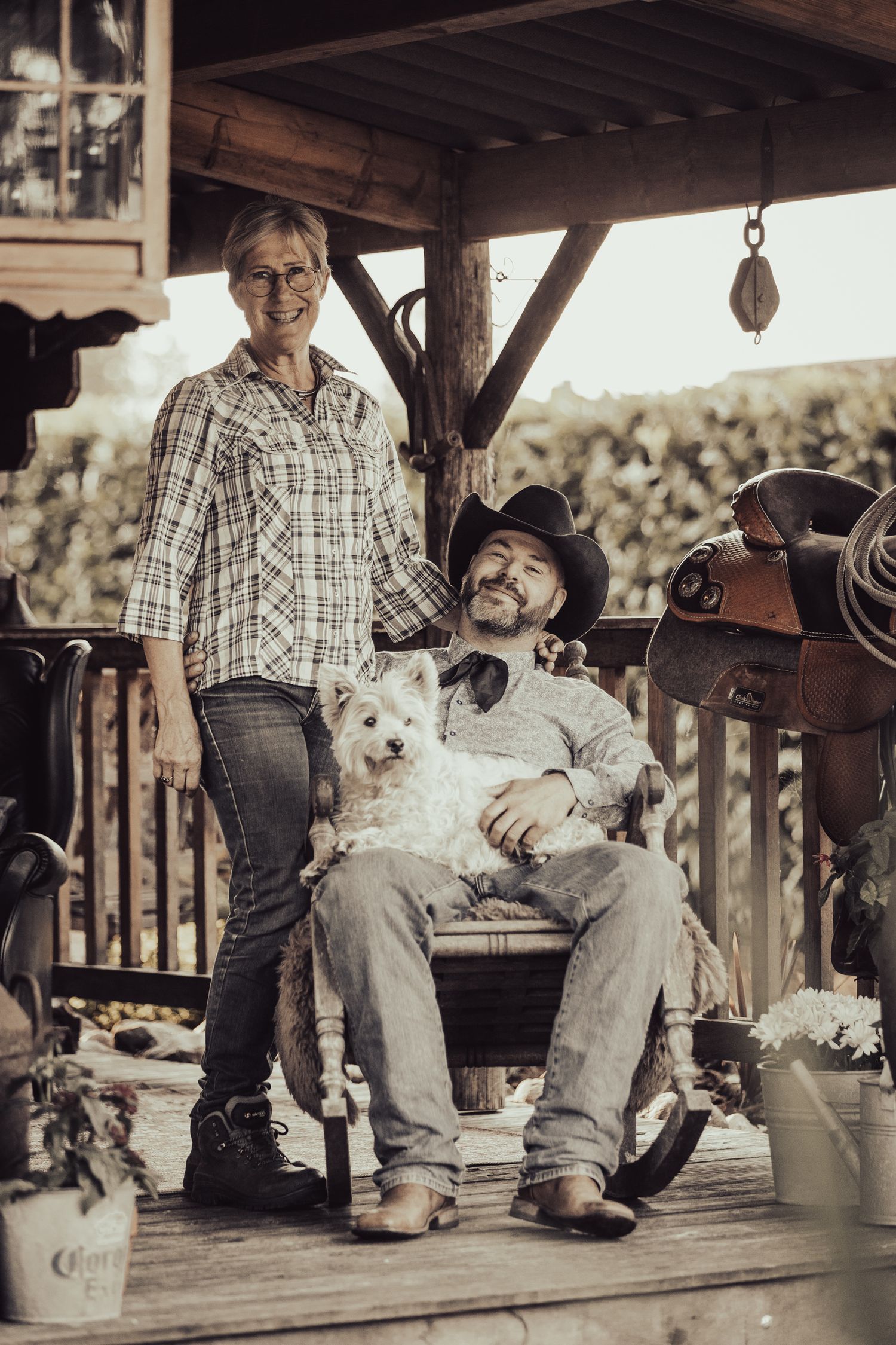 A rustic scene on a wooden porch with western saddles and ranch equipment.