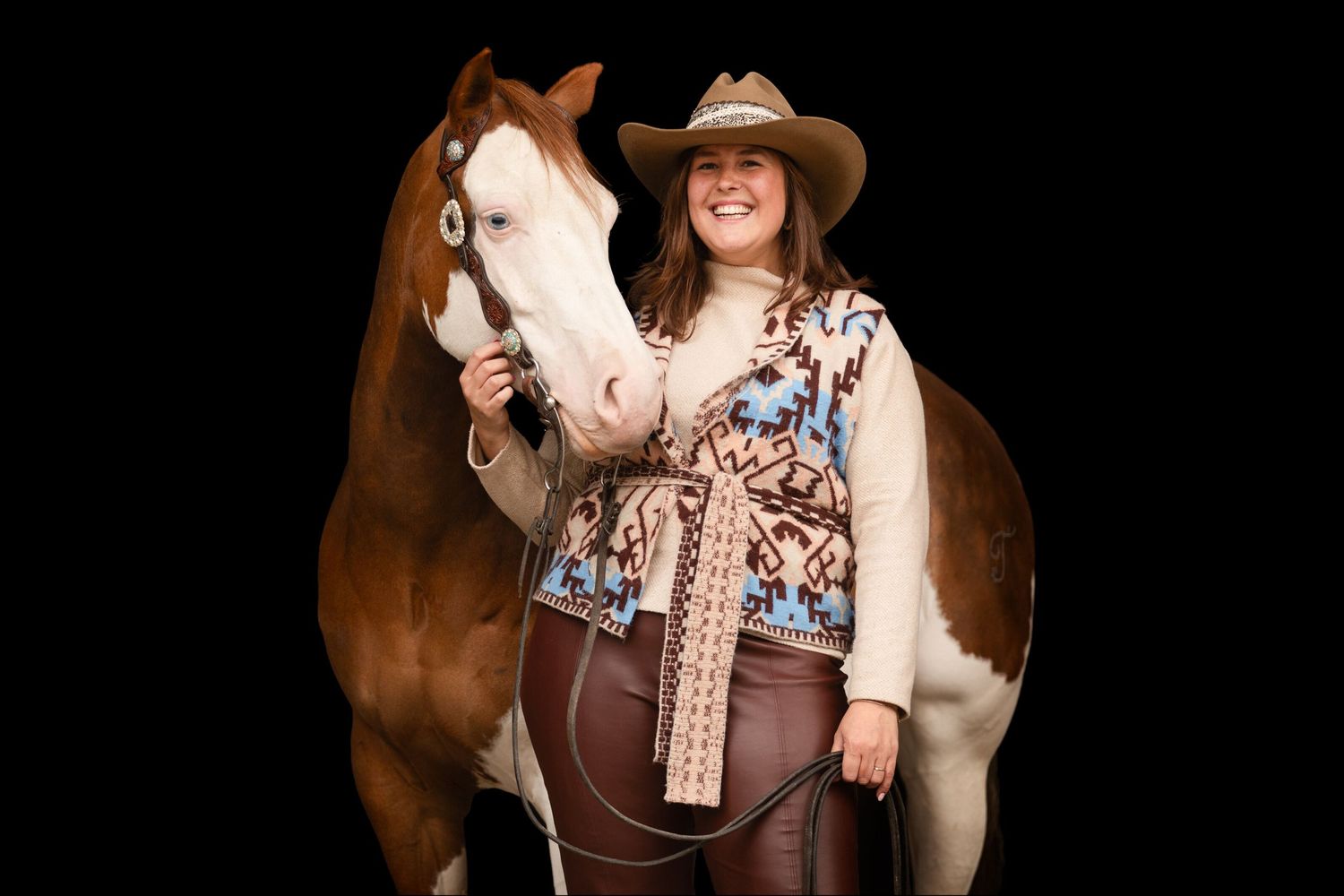 Western themed equestrian portrait session against dark background with brown horse.