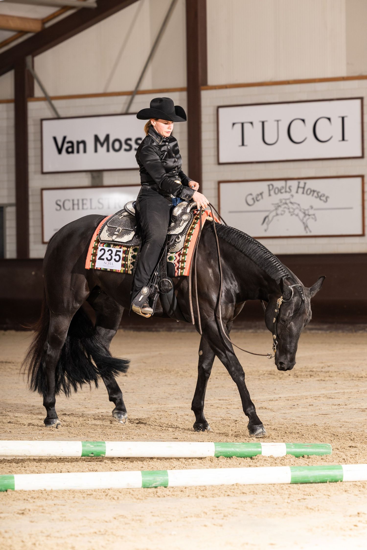 Black horse and rider performing precise movements around green poles in indoor arena.