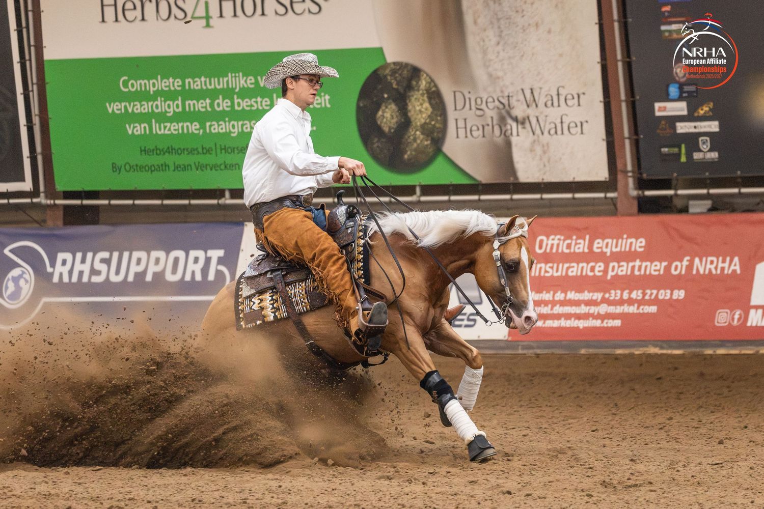 Reining horse and rider performing a sliding stop in an indoor arena during an NRHA equestrian competition.