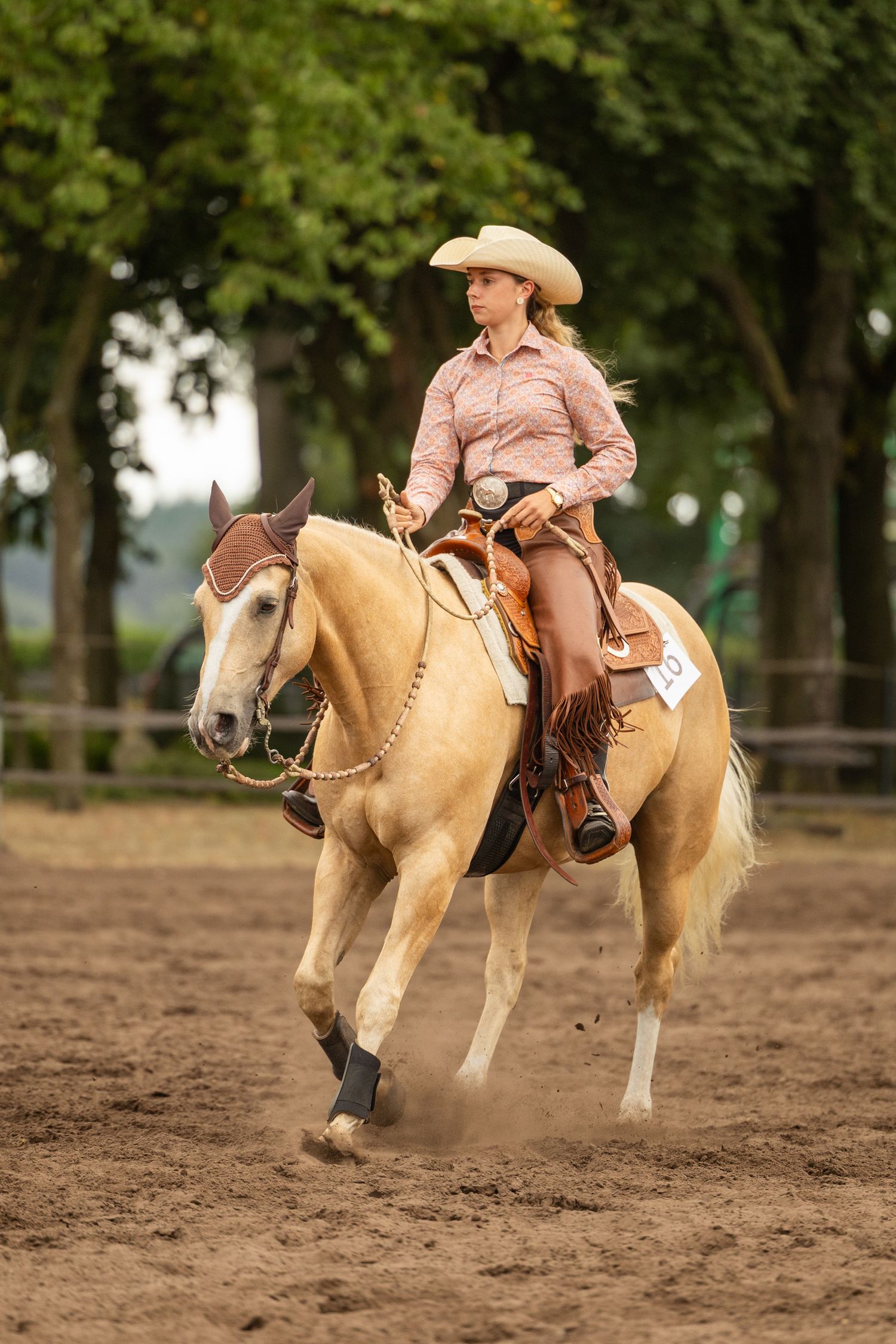 A palomino horse and rider perform in a western riding arena.
