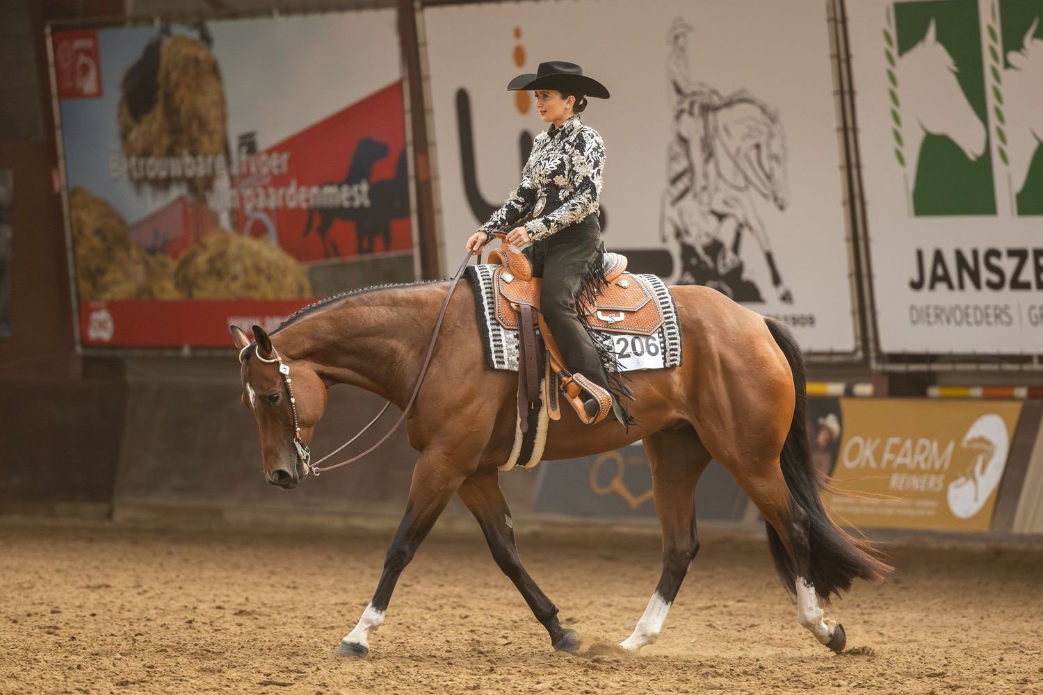 Western rider guiding bay horse through competition pattern in indoor arena setting.