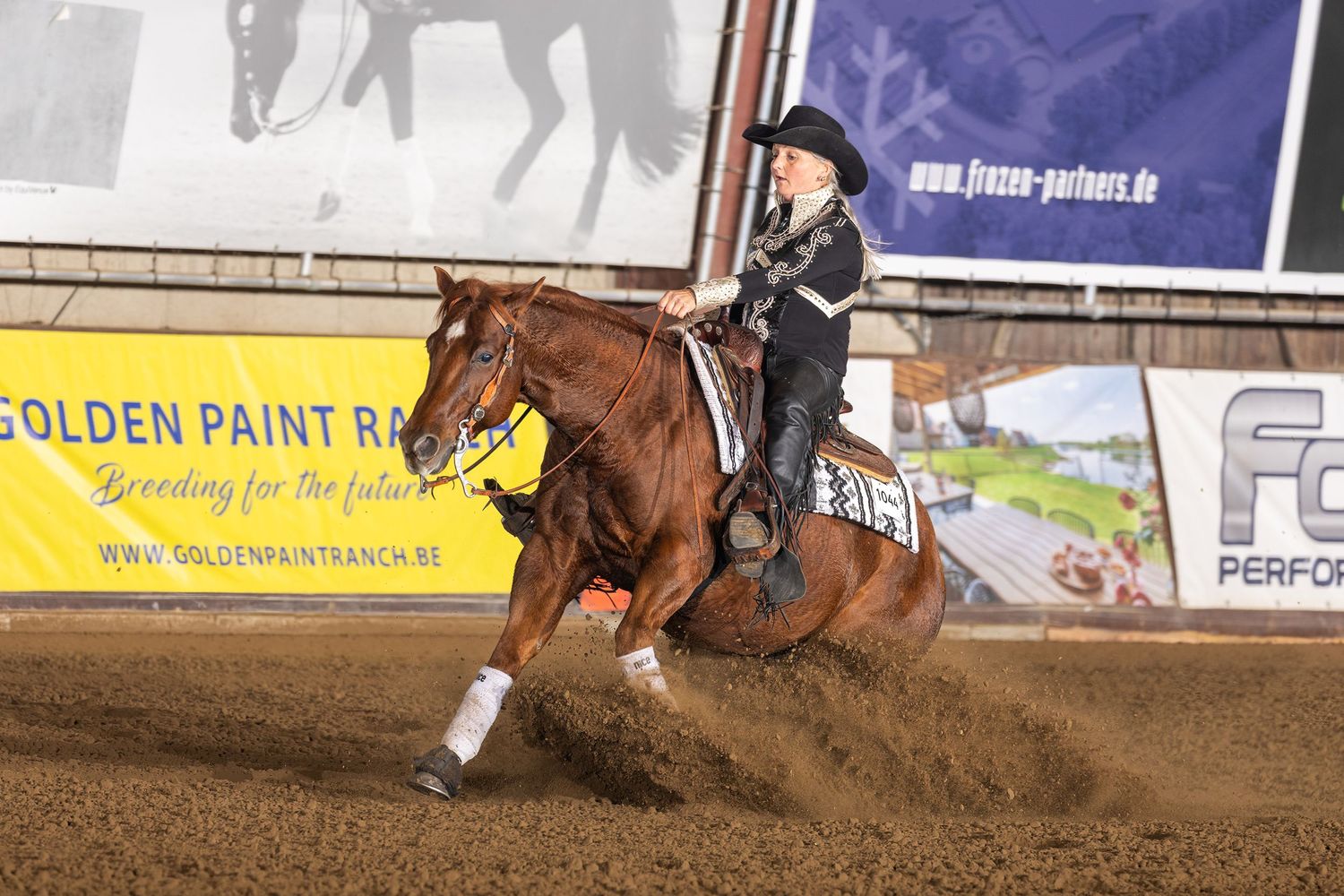 Western rider guides chestnut horse through reining pattern in sandy indoor arena.