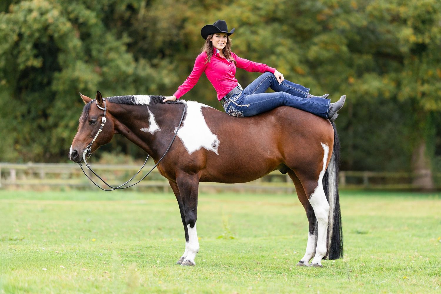 Paint horse with rider demonstrating trick riding pose in field.