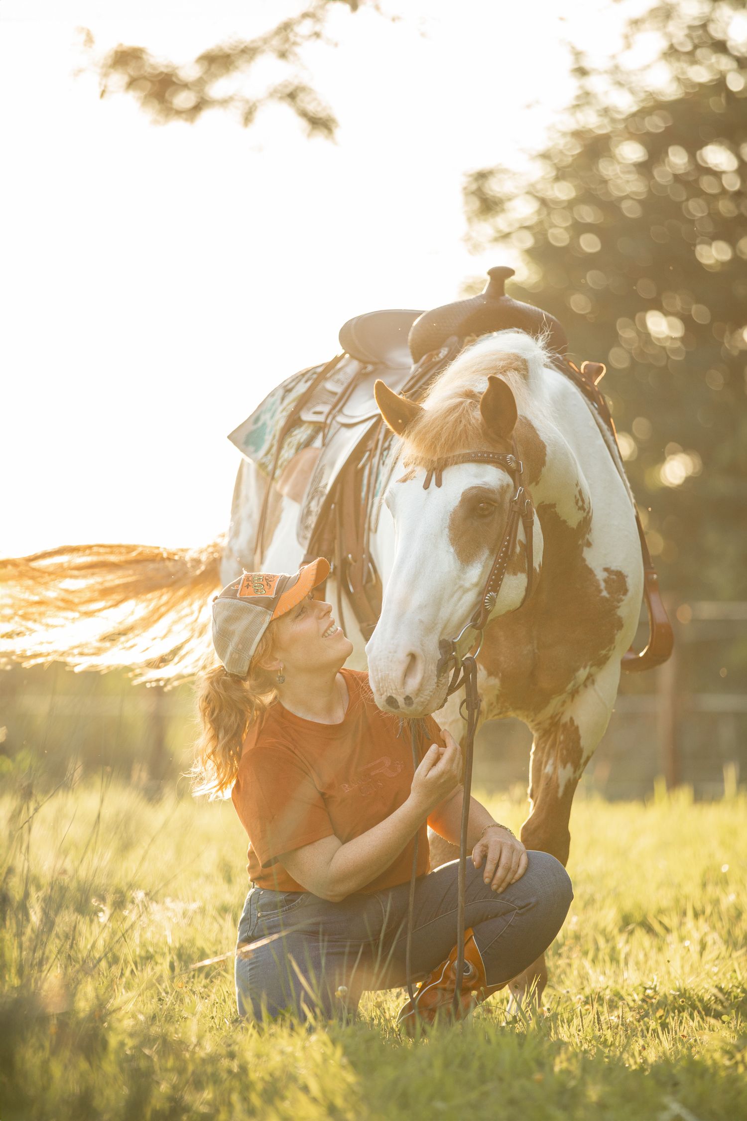 Paint horse and rider bonding in sunlit meadow during golden hour.