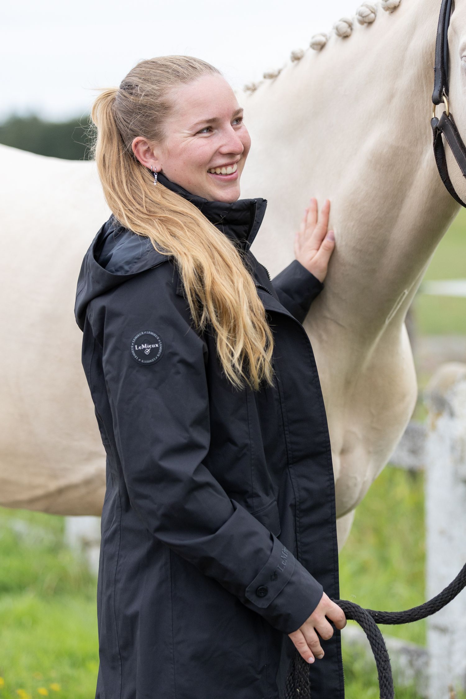 Handler in black jacket working with a light-colored horse in an outdoor arena.