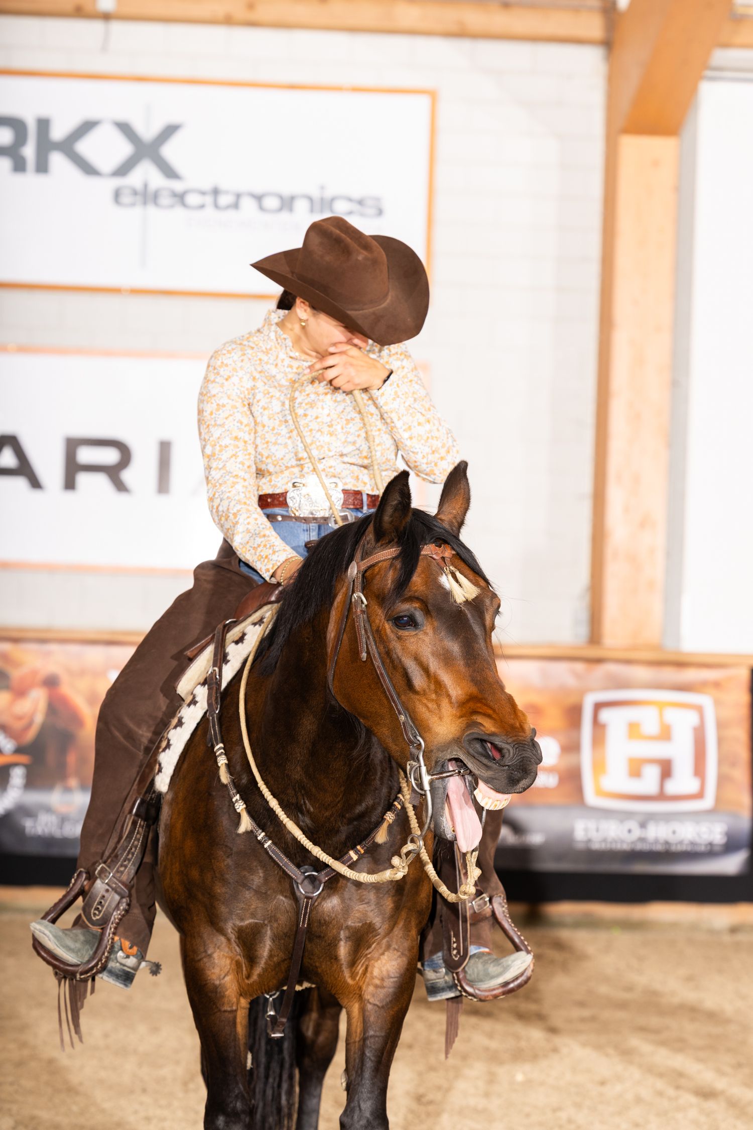 Horses and riders in western attire performing in an indoor arena with sponsor signage.