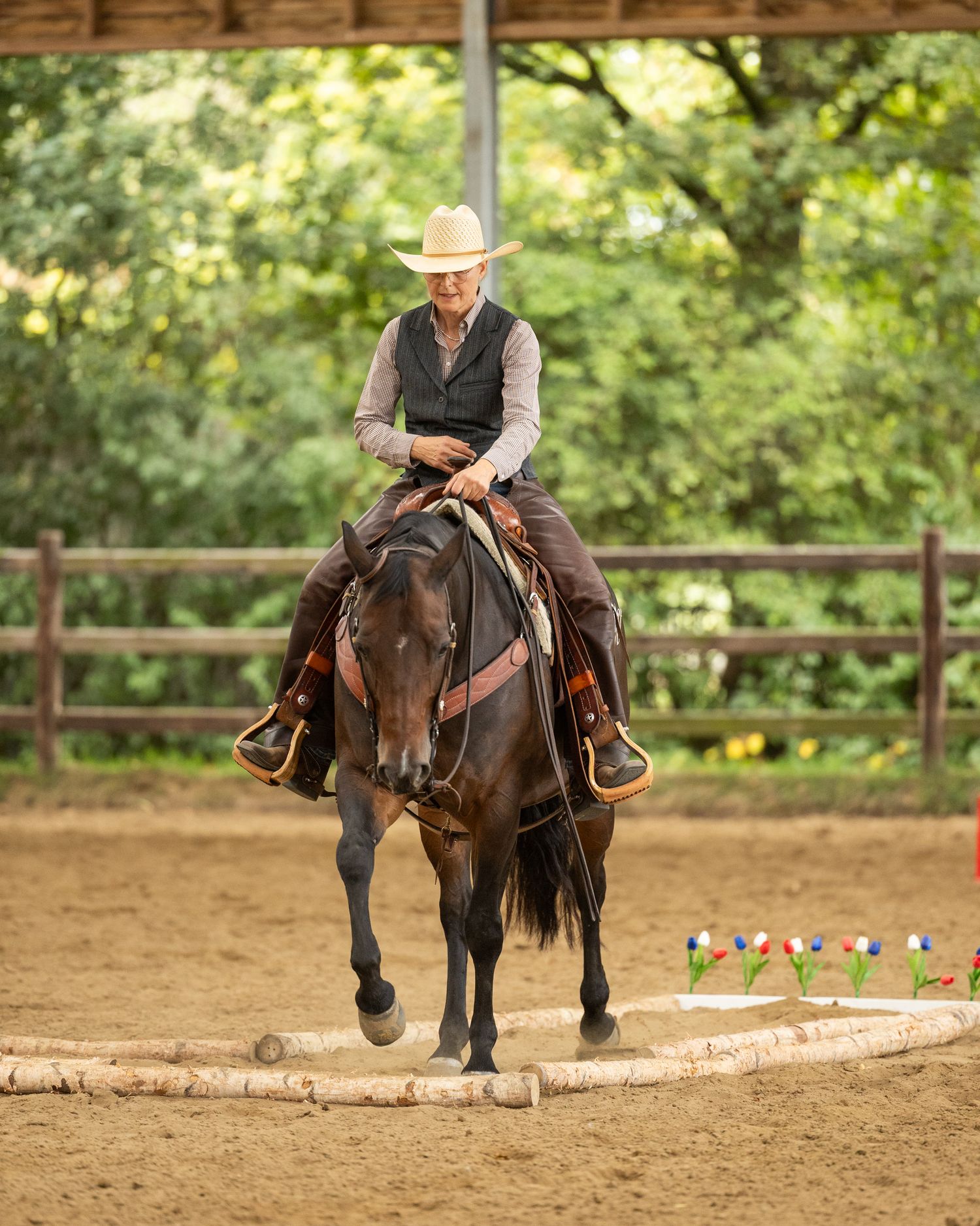 Rider in western attire jumping horse over ground poles in covered arena.