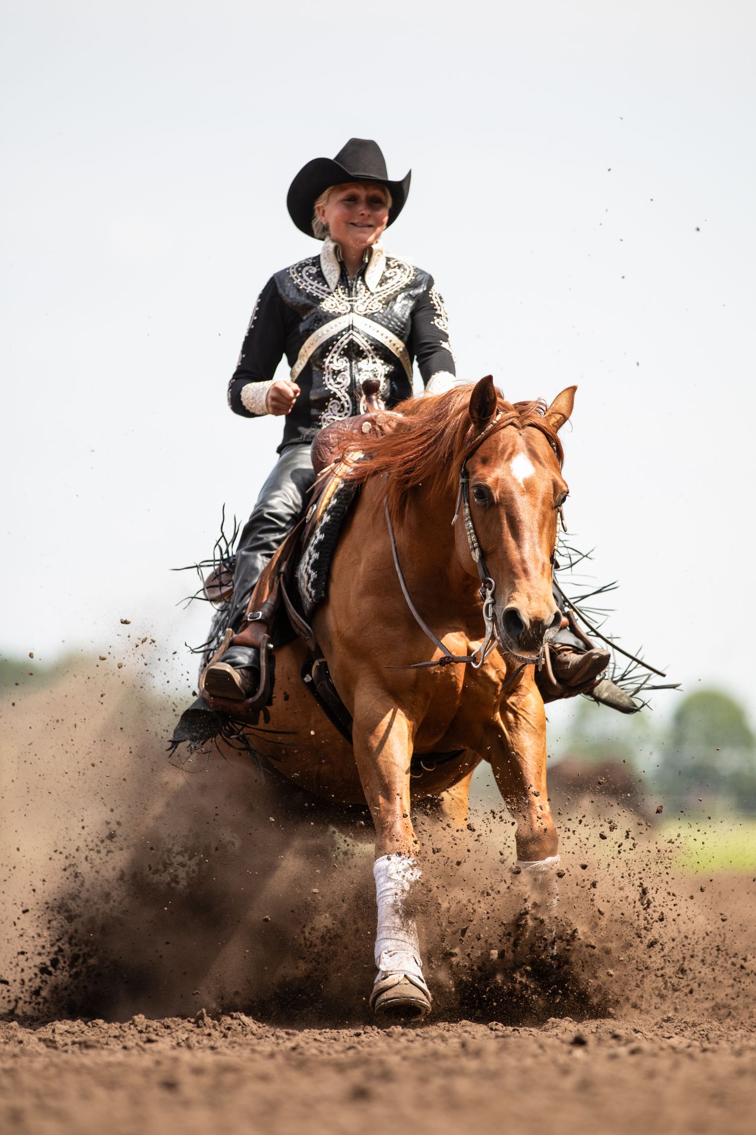 Western rider performs dramatic reining stop on chestnut horse kicking up arena dirt.