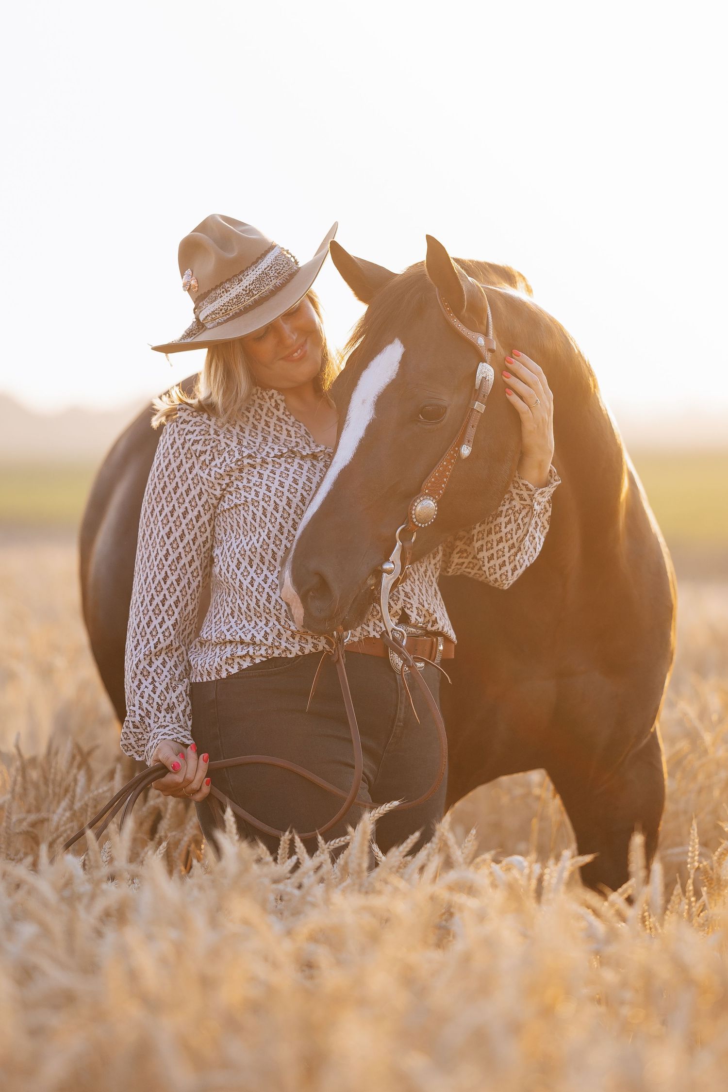 Woman in cowboy hat bonding with dark horse in golden wheat field at sunset.