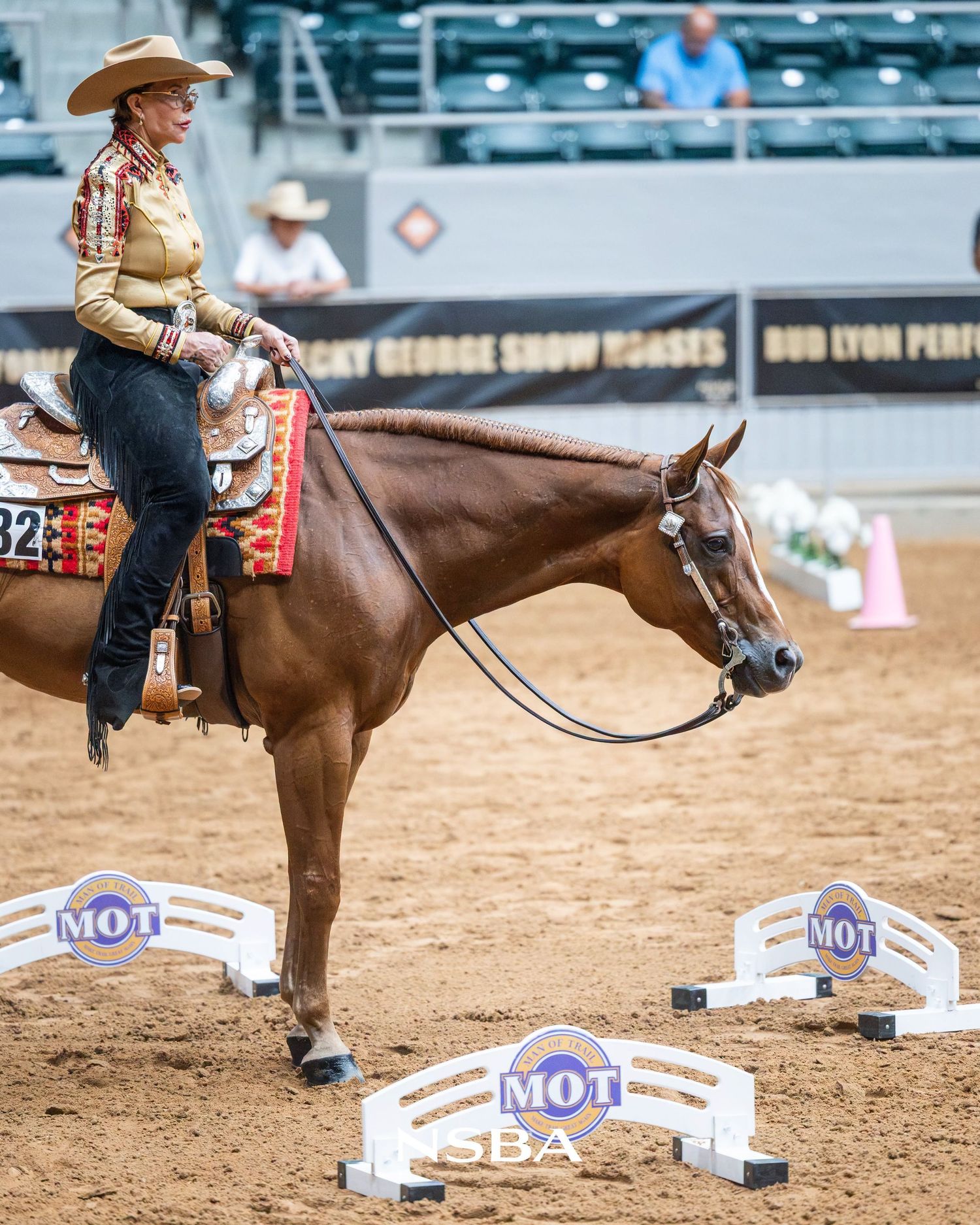 Woman in western attire riding a chestnut horse at an indoor equestrian competition with MOT SBA barriers.